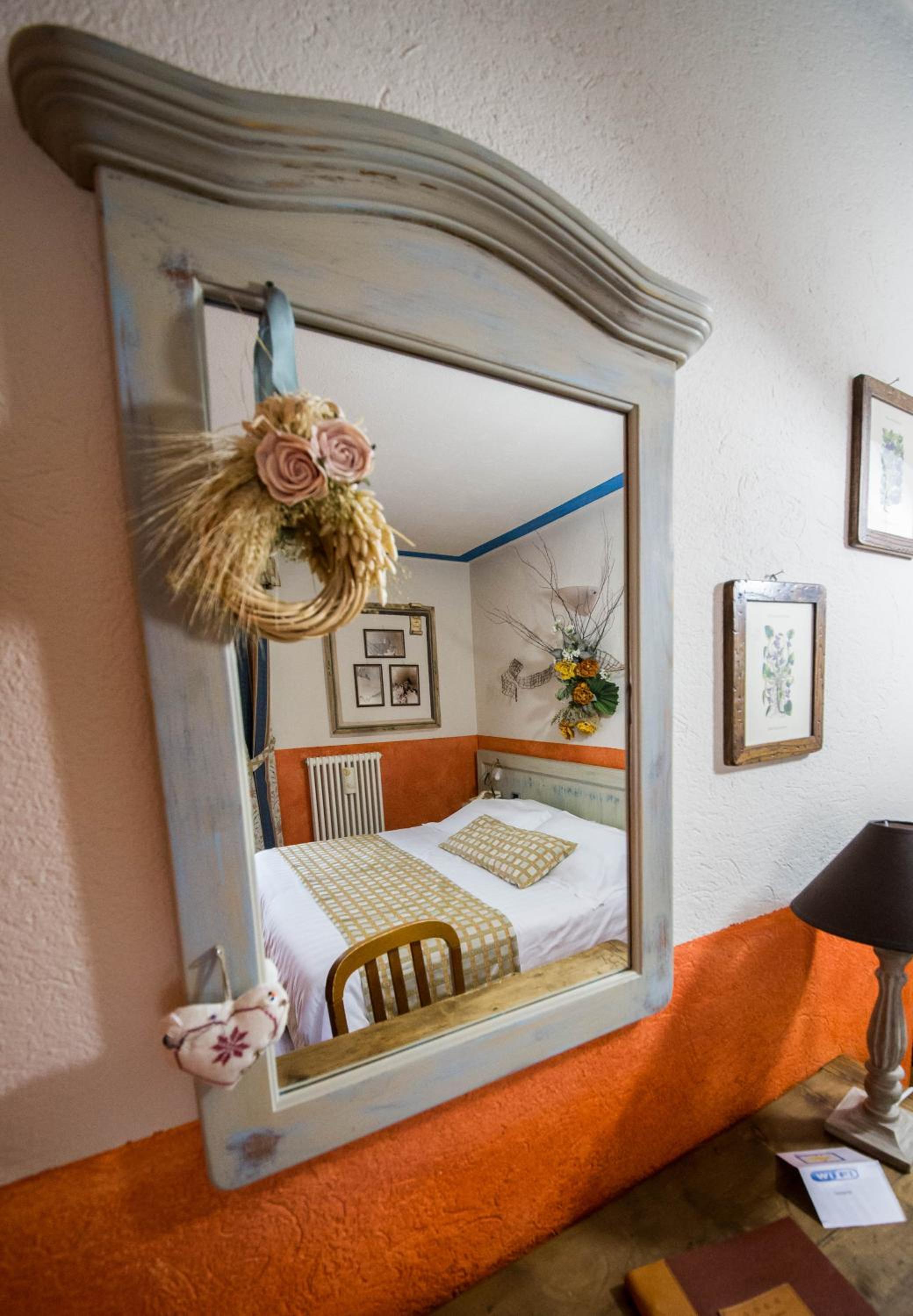 Rustic mirror reflecting a double bed, orange walls, and dried flower decor