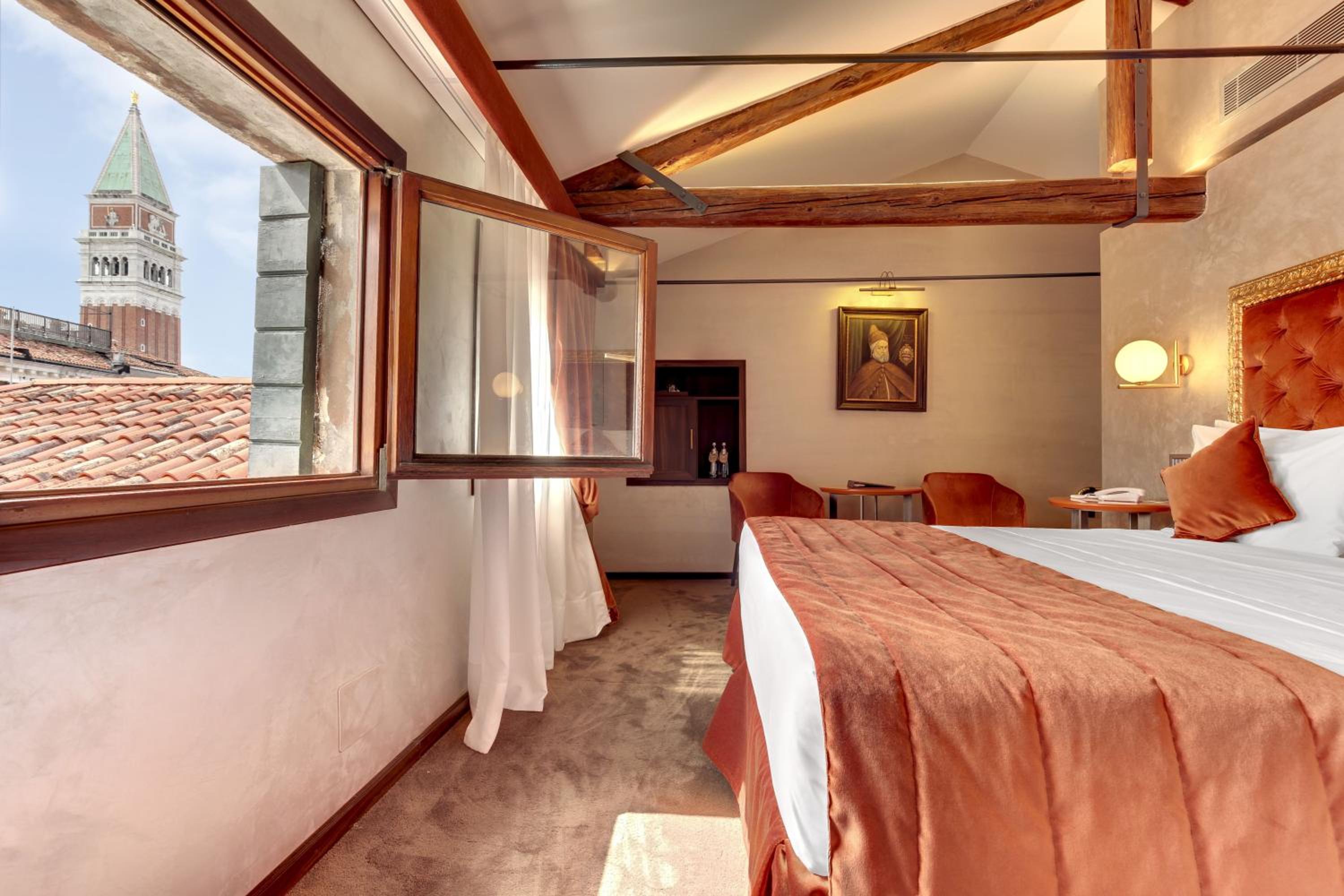 Hotel room with a bed, wooden beams, and a window view of a tower.