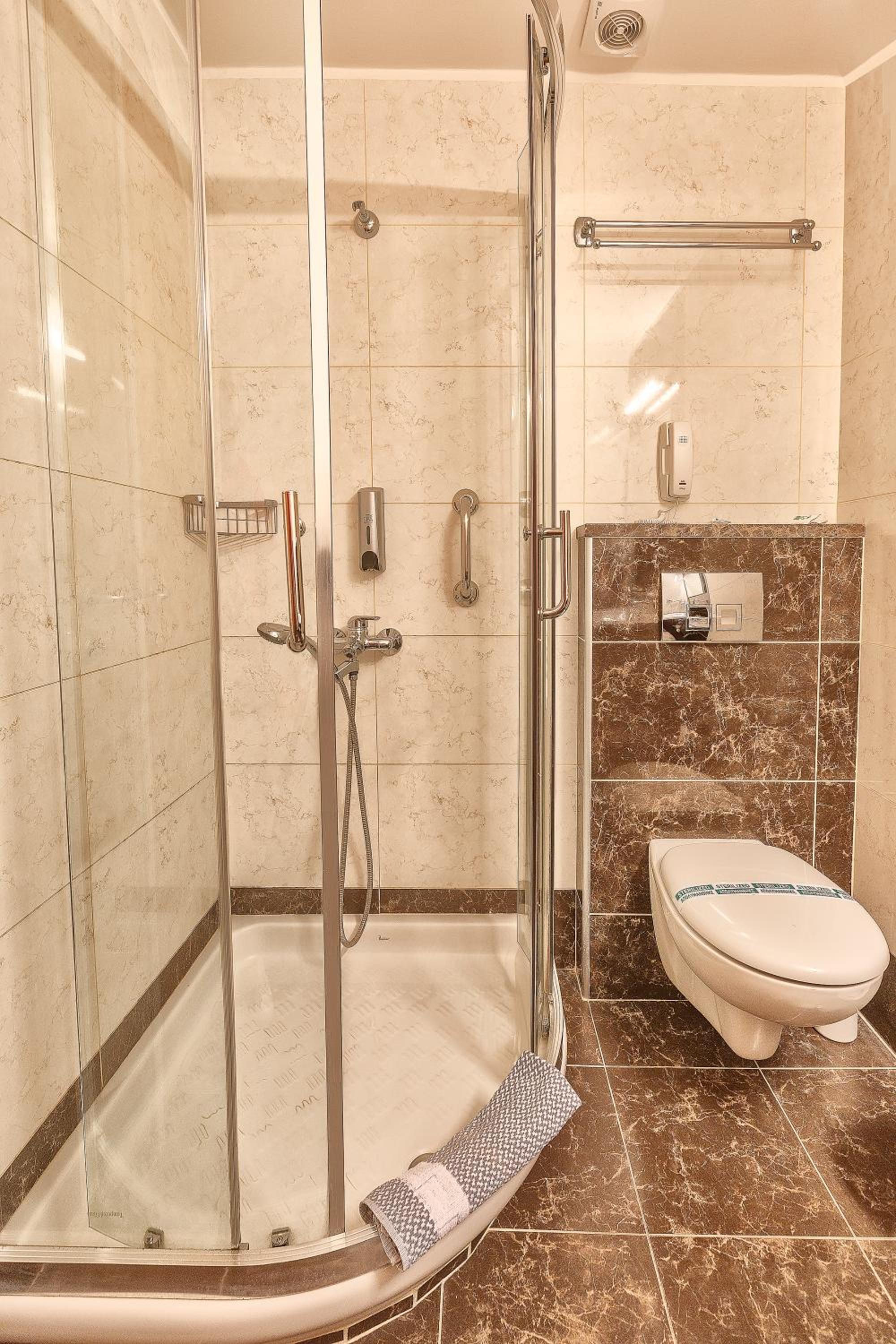 Bathroom with a glass-enclosed shower, white toilet, and brown marble tiles.