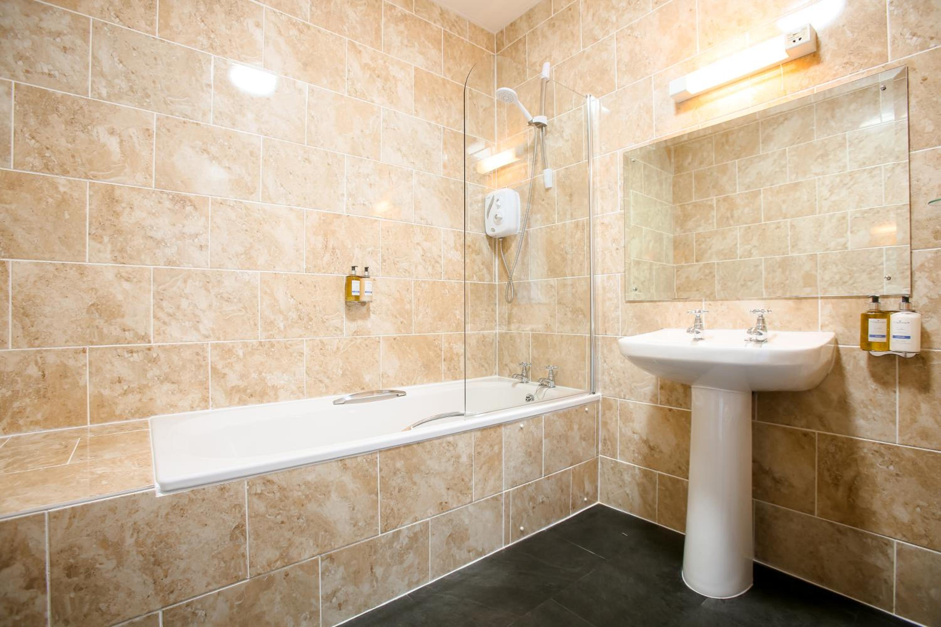 Beige tiled bathroom with bathtub, glass shower screen and pedestal sink