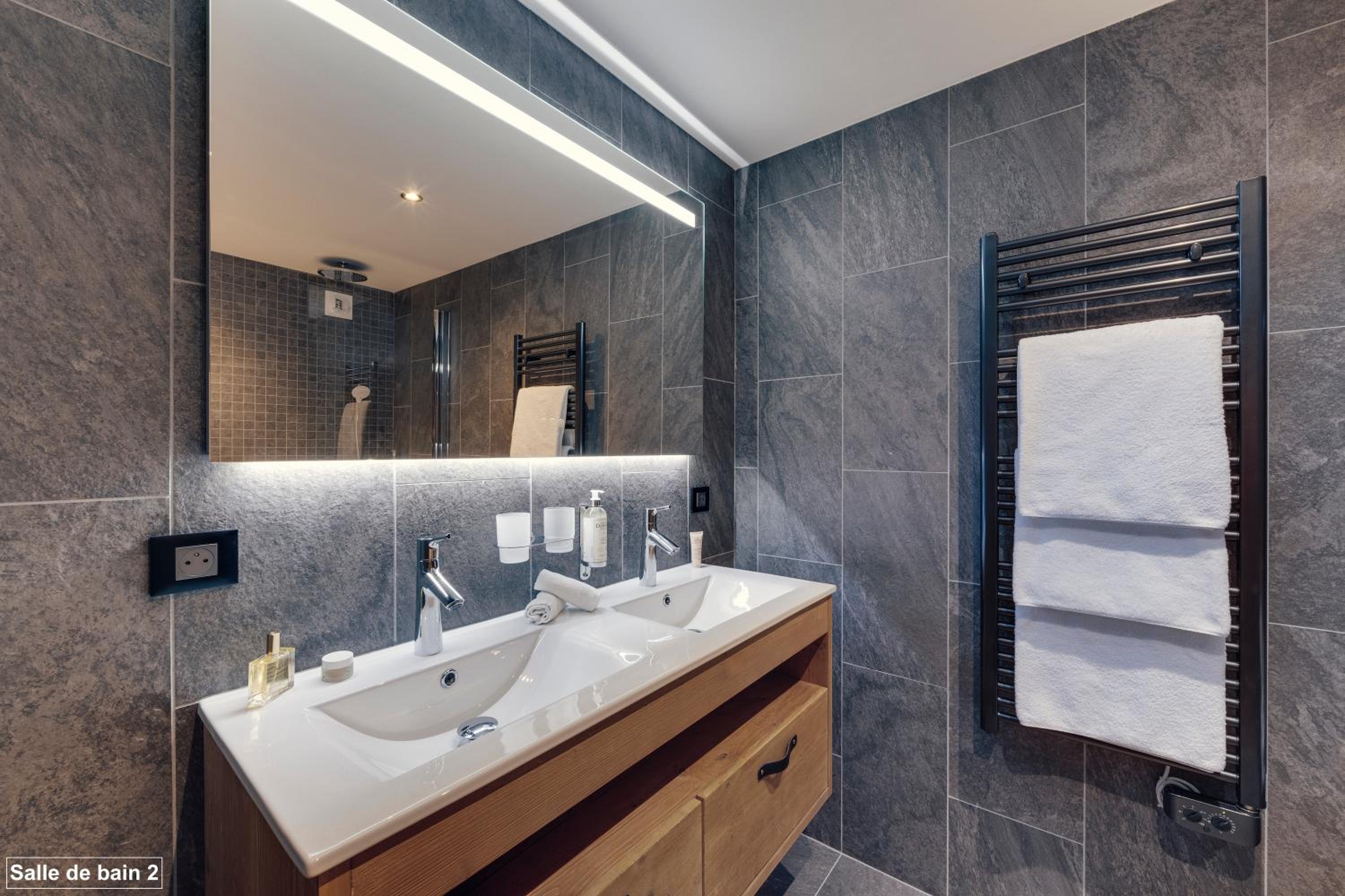 Bathroom with a double sink vanity, large mirror, and dark gray tiled walls.