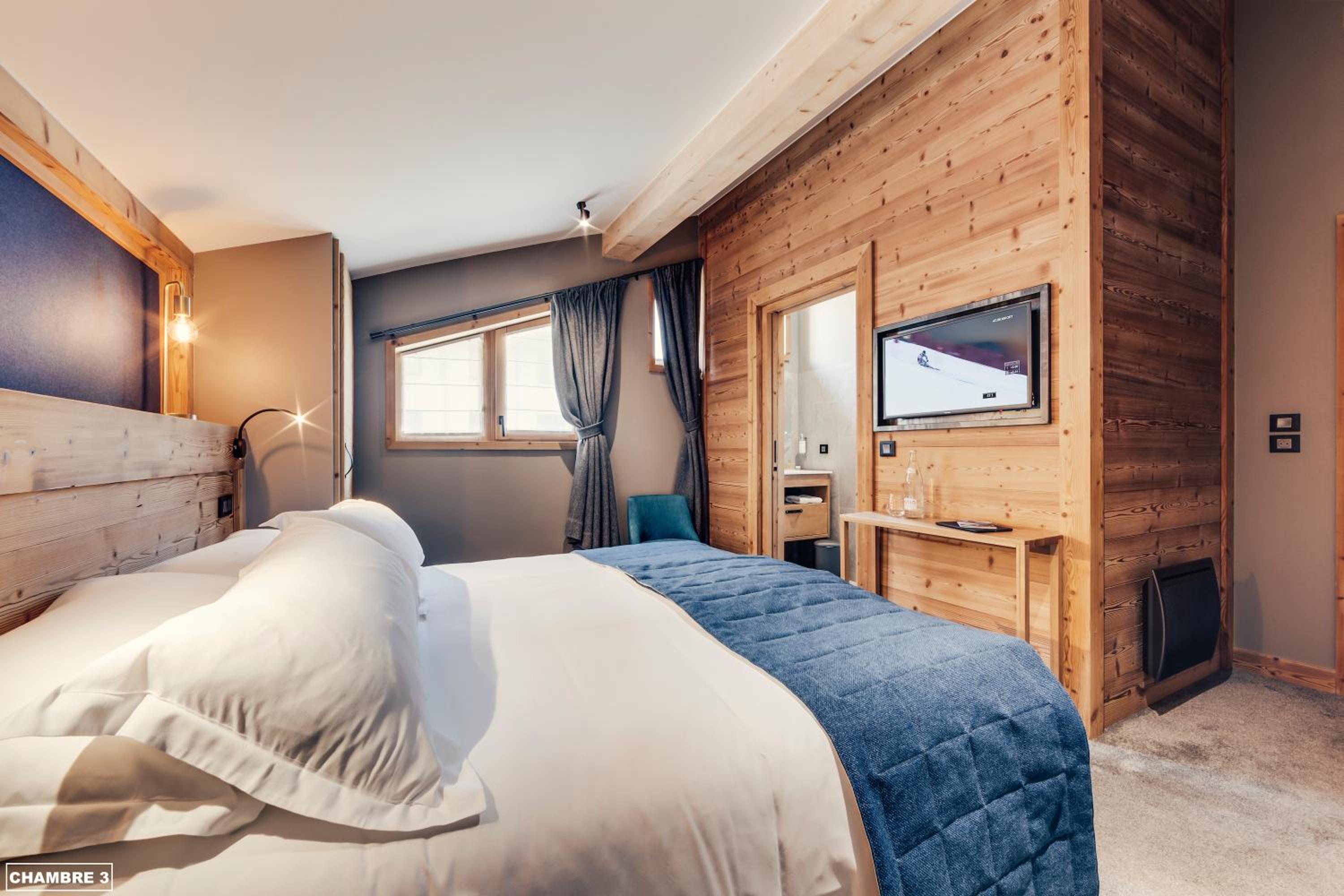 Hotel bedroom with a large bed, wooden wall paneling, and a mounted television.