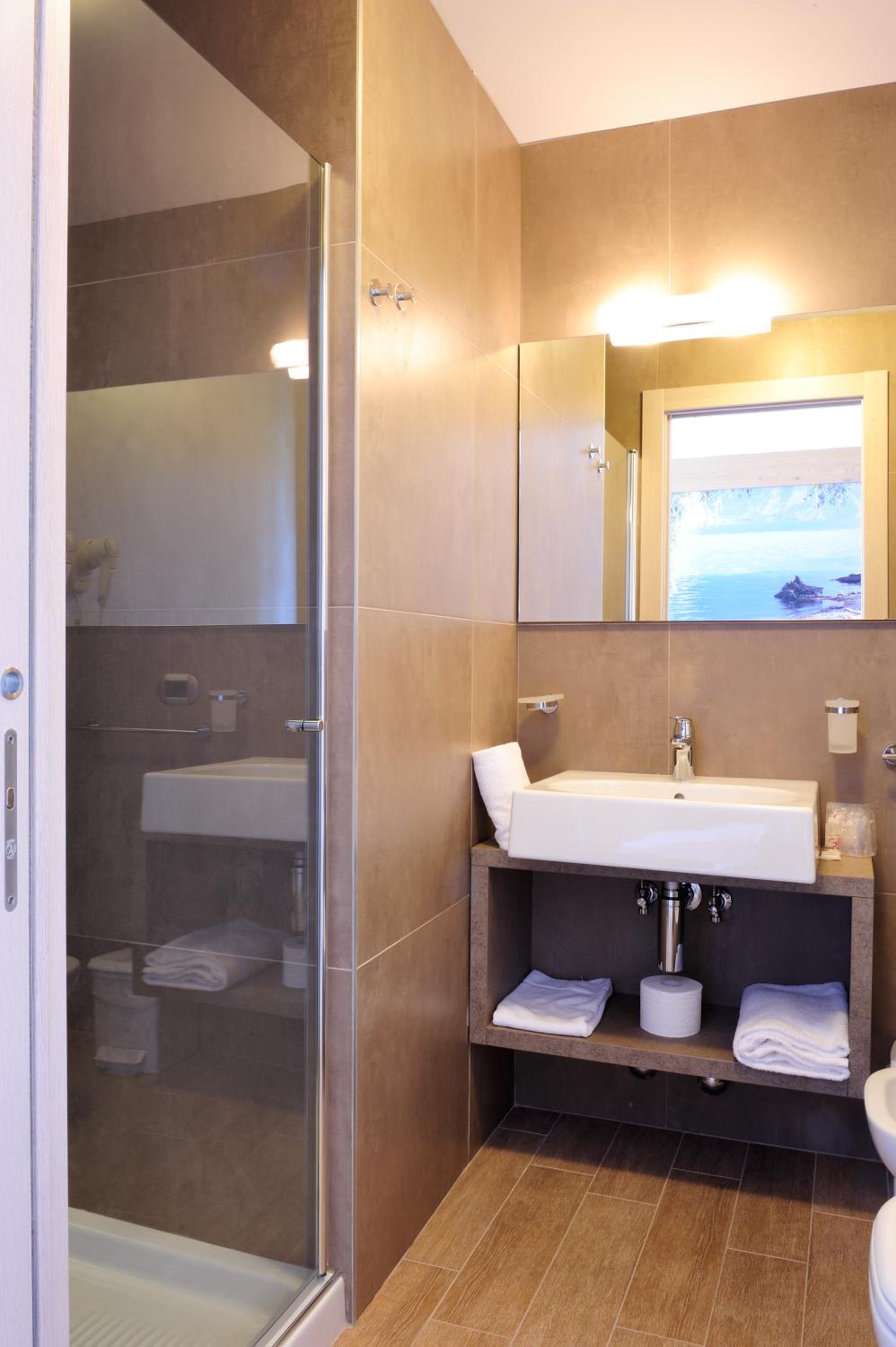 Modern bathroom with glass shower, white sink, open shelf with towels