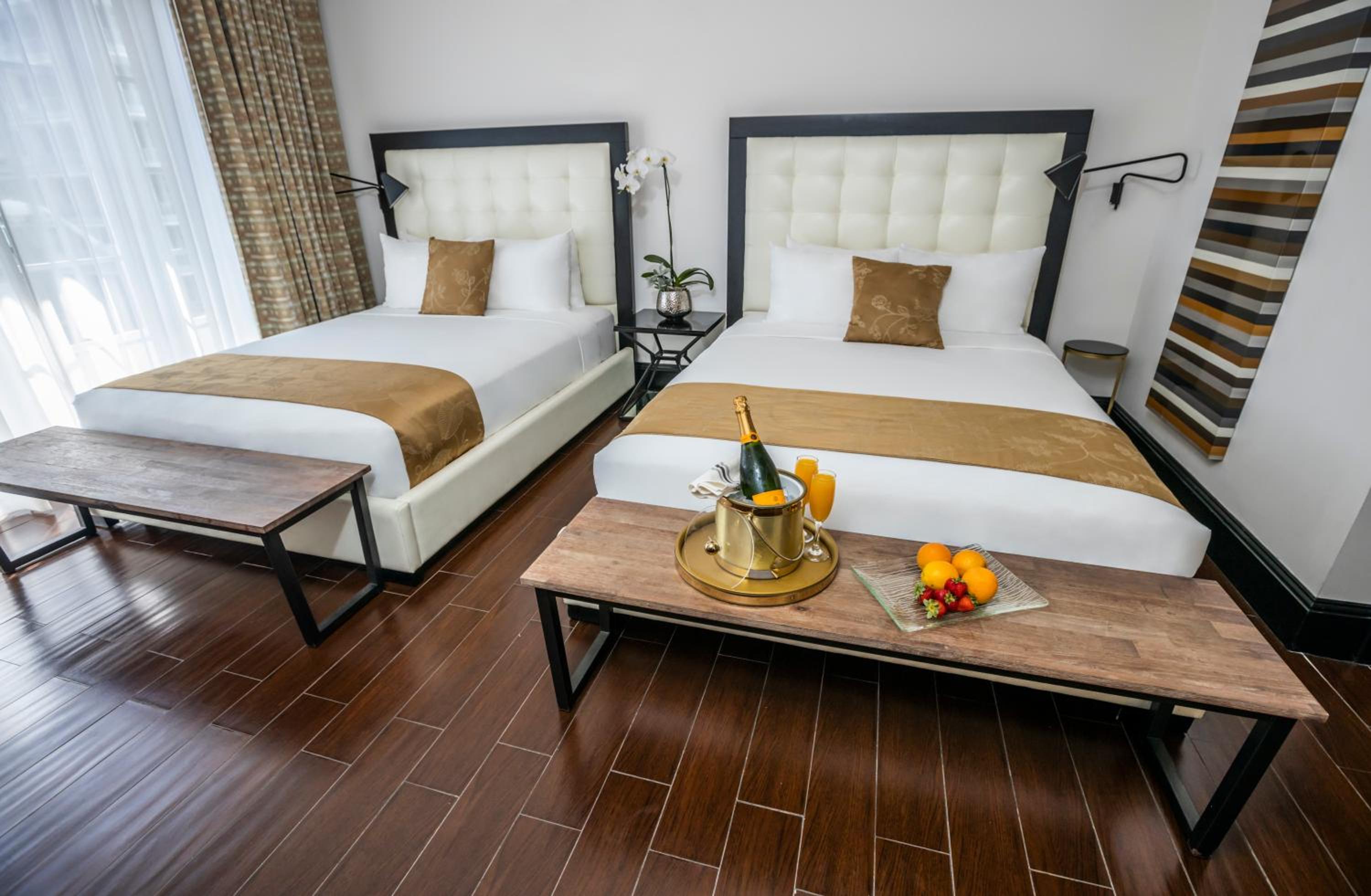 Hotel room with two double beds, white linens, and a wooden table with fruit.