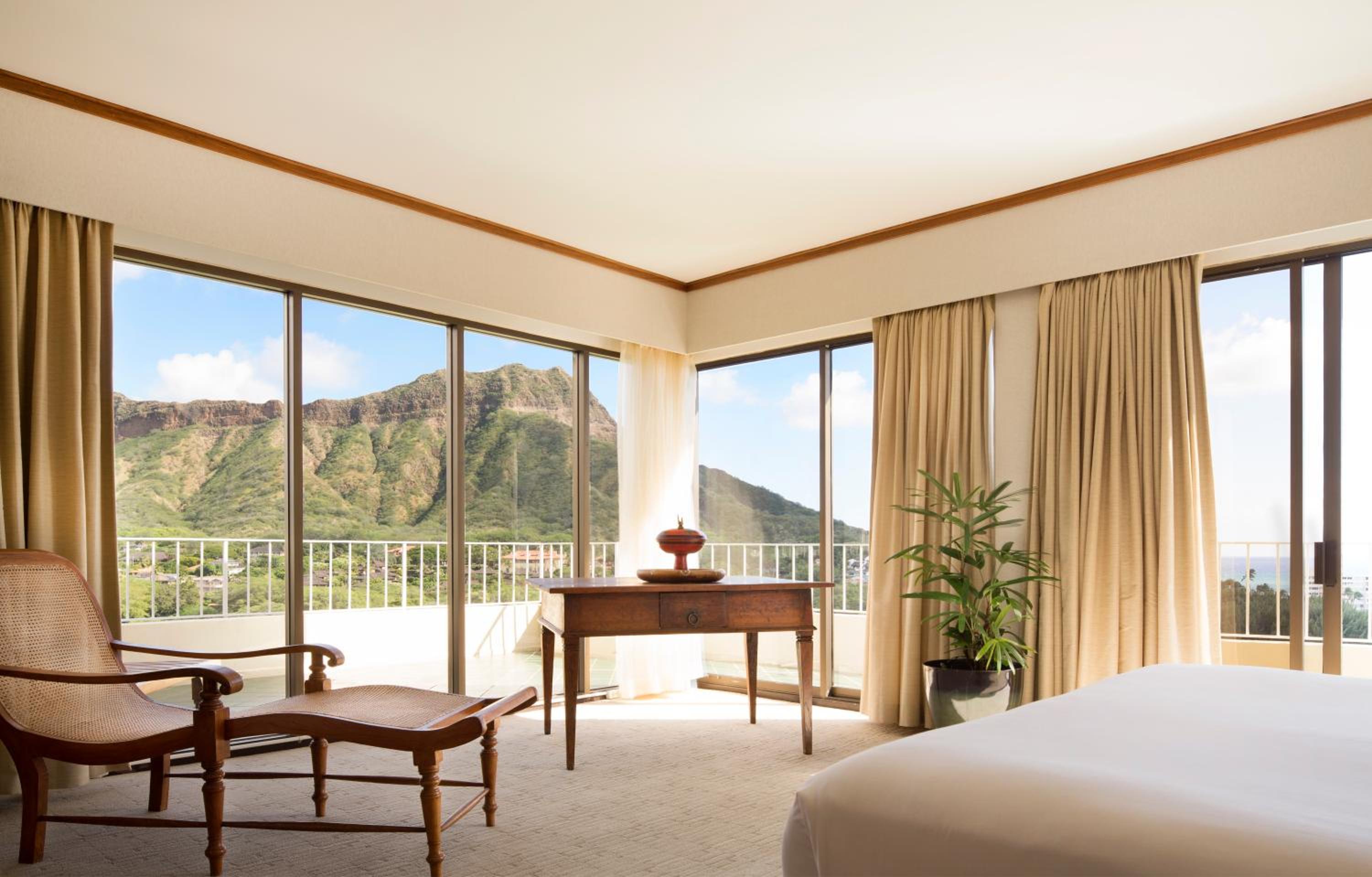 Hotel room with a chaise lounge and desk facing large windows with a mountain view.