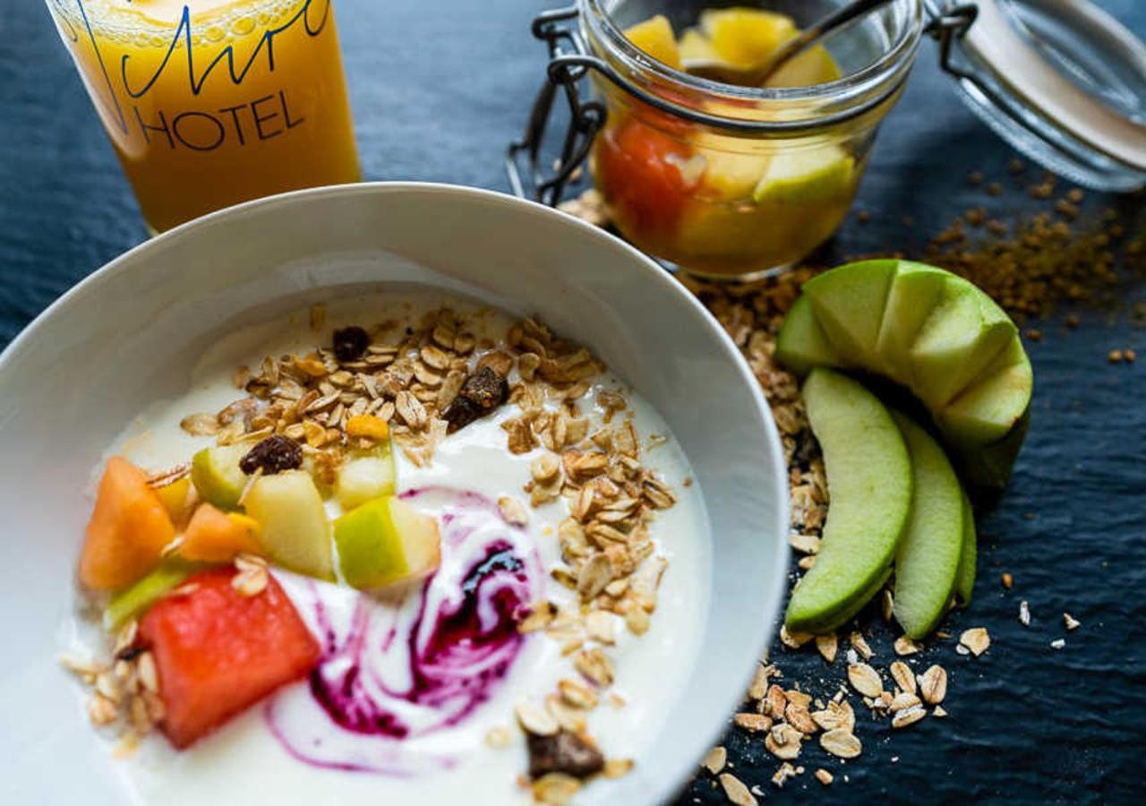 Breakfast bowl with yogurt, granola, and fruit slices next to a juice glass.