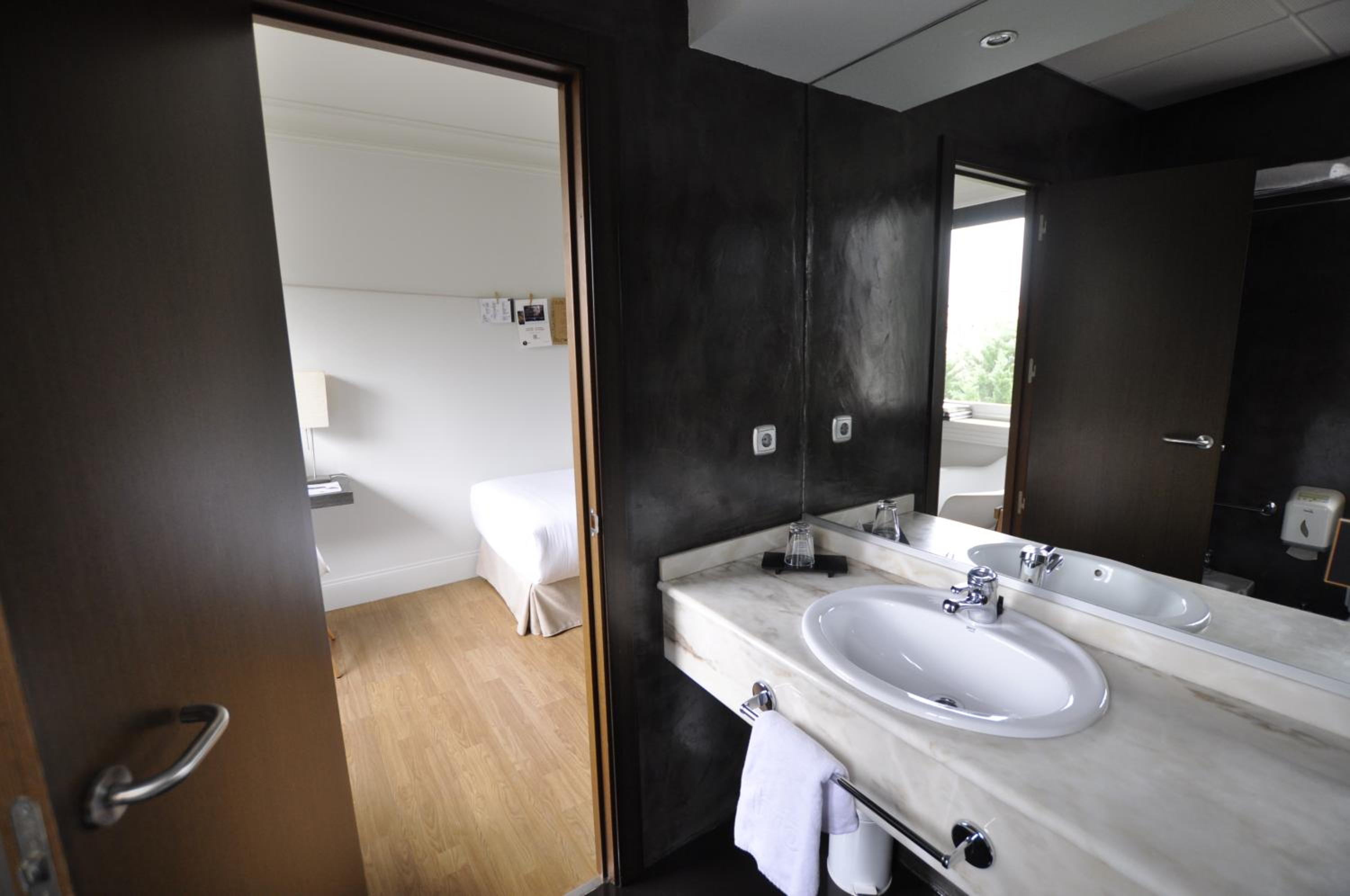 Bathroom with a white marble sink and mirror, opening to a bedroom with a bed.
