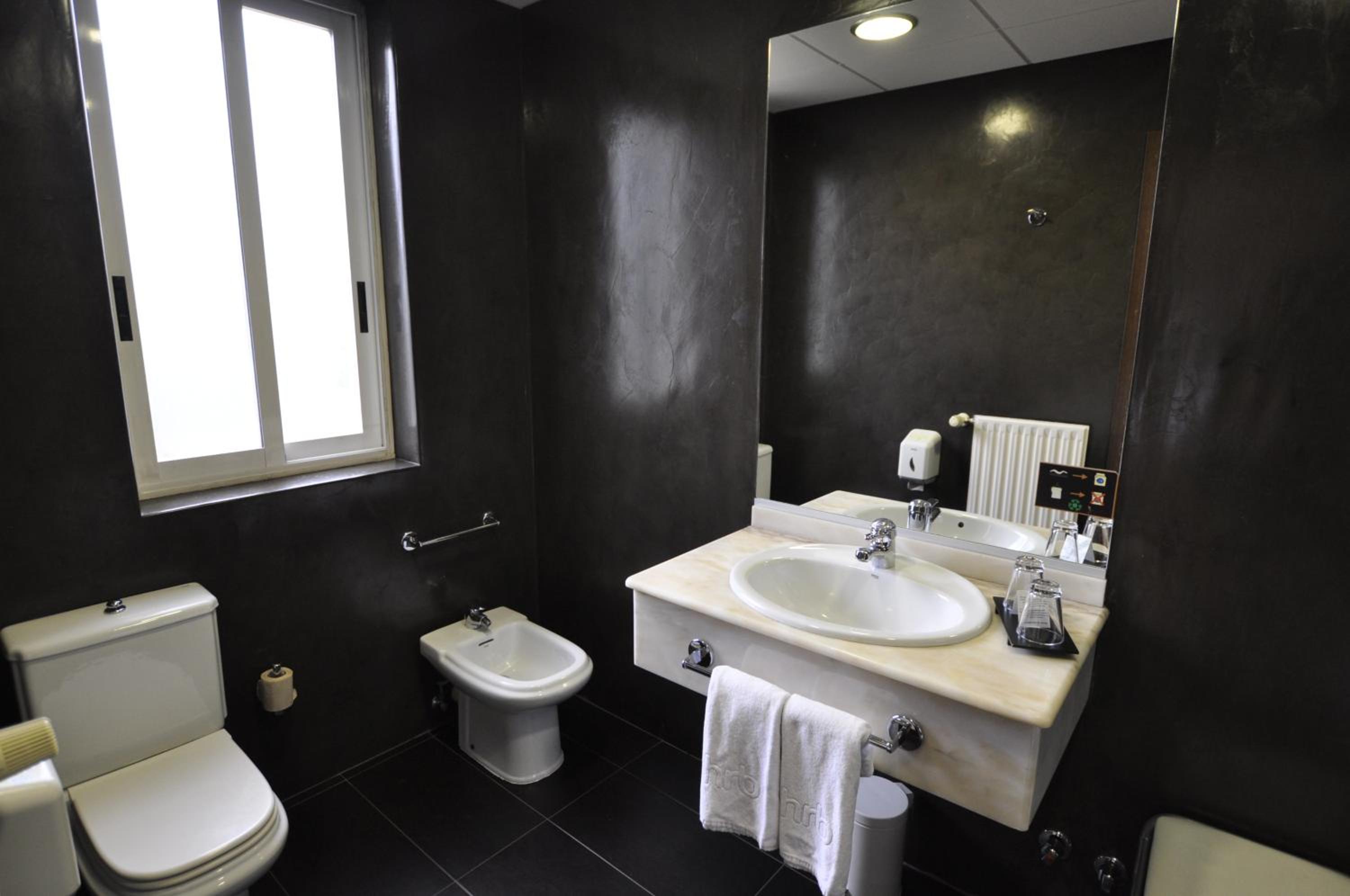 Bathroom with black walls, white toilet, bidet, and a marble vanity sink.
