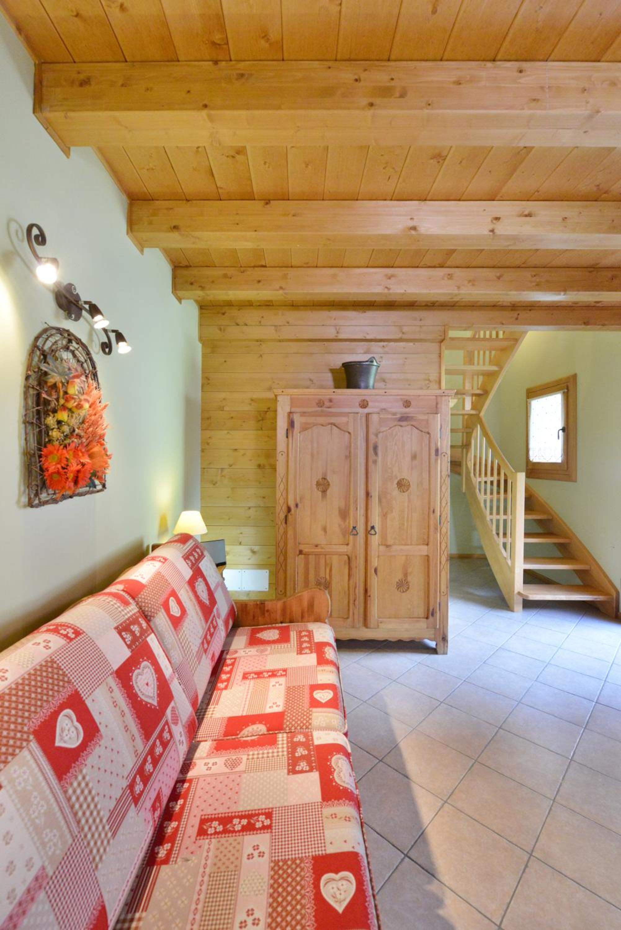 Living area with a red and white patterned sofa, wooden ceiling, and tiled floor.