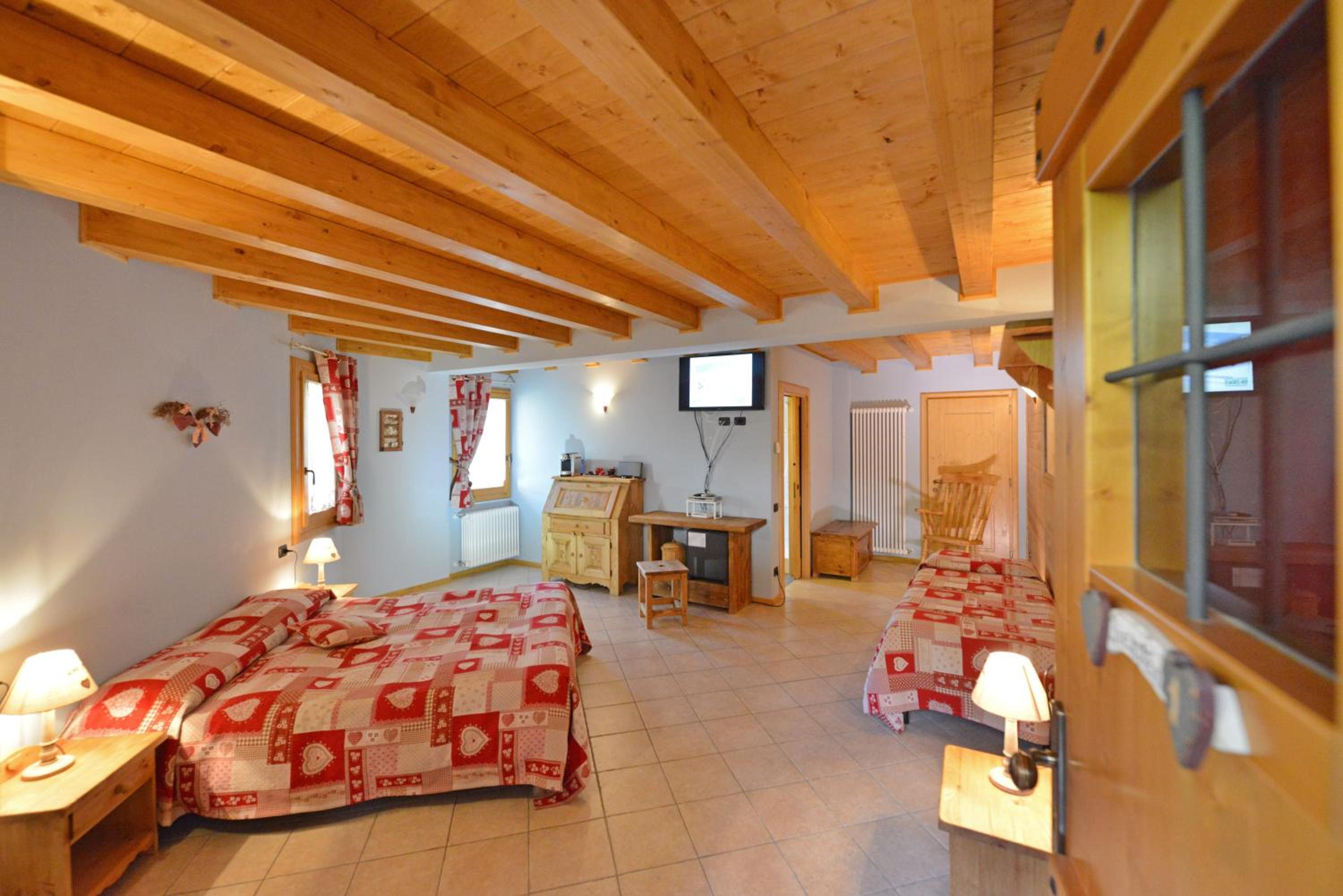 Hotel room with two beds, wooden ceiling beams, and a small desk area.