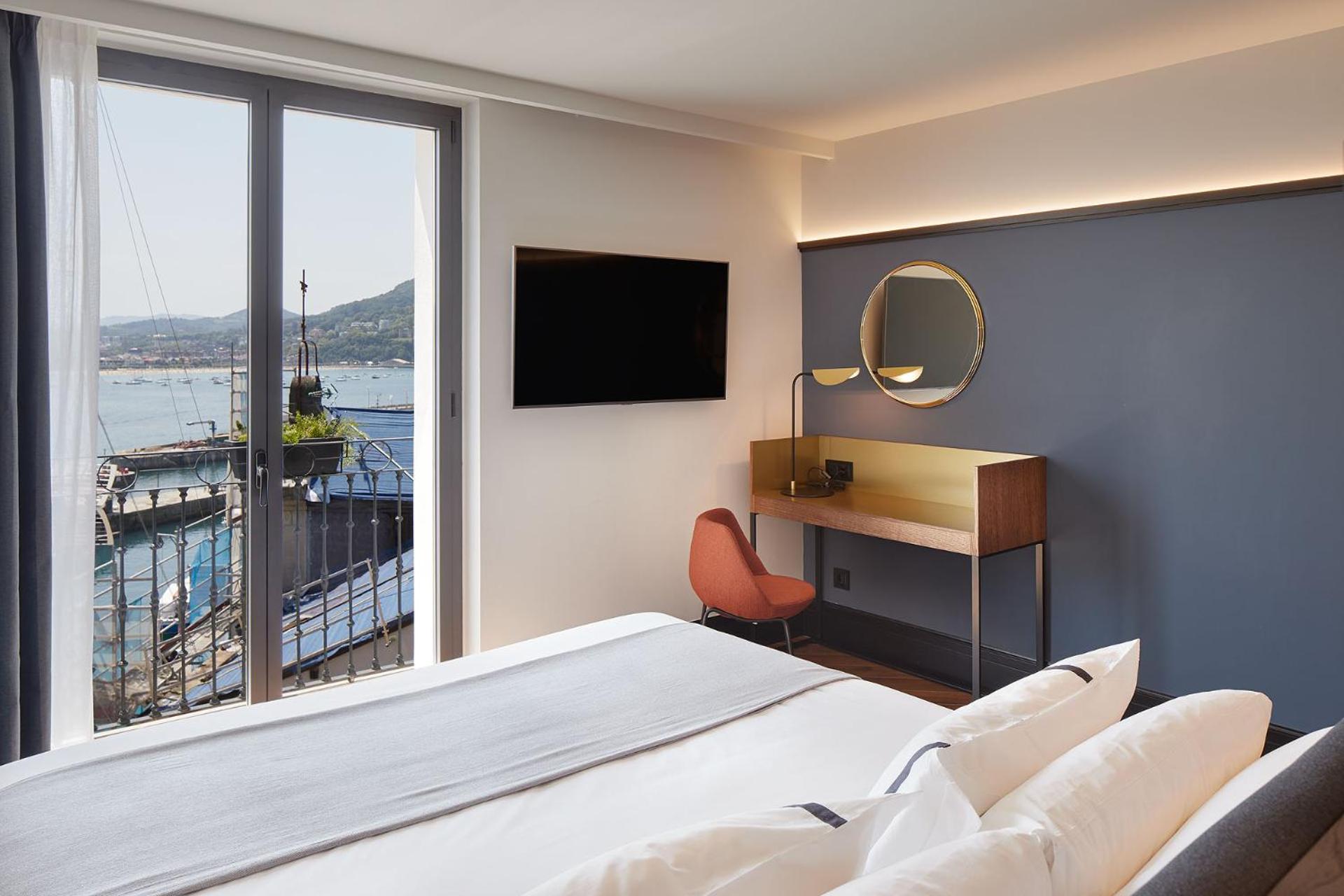 Modern bedroom with desk, wall TV and balcony door overlooking a harbor