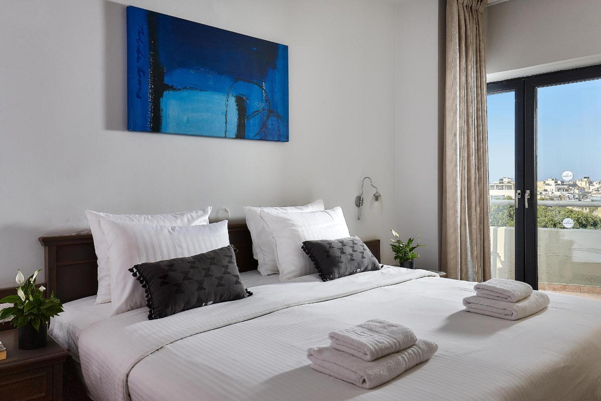Bedroom with a double bed, white linens, and a large blue painting on the wall.