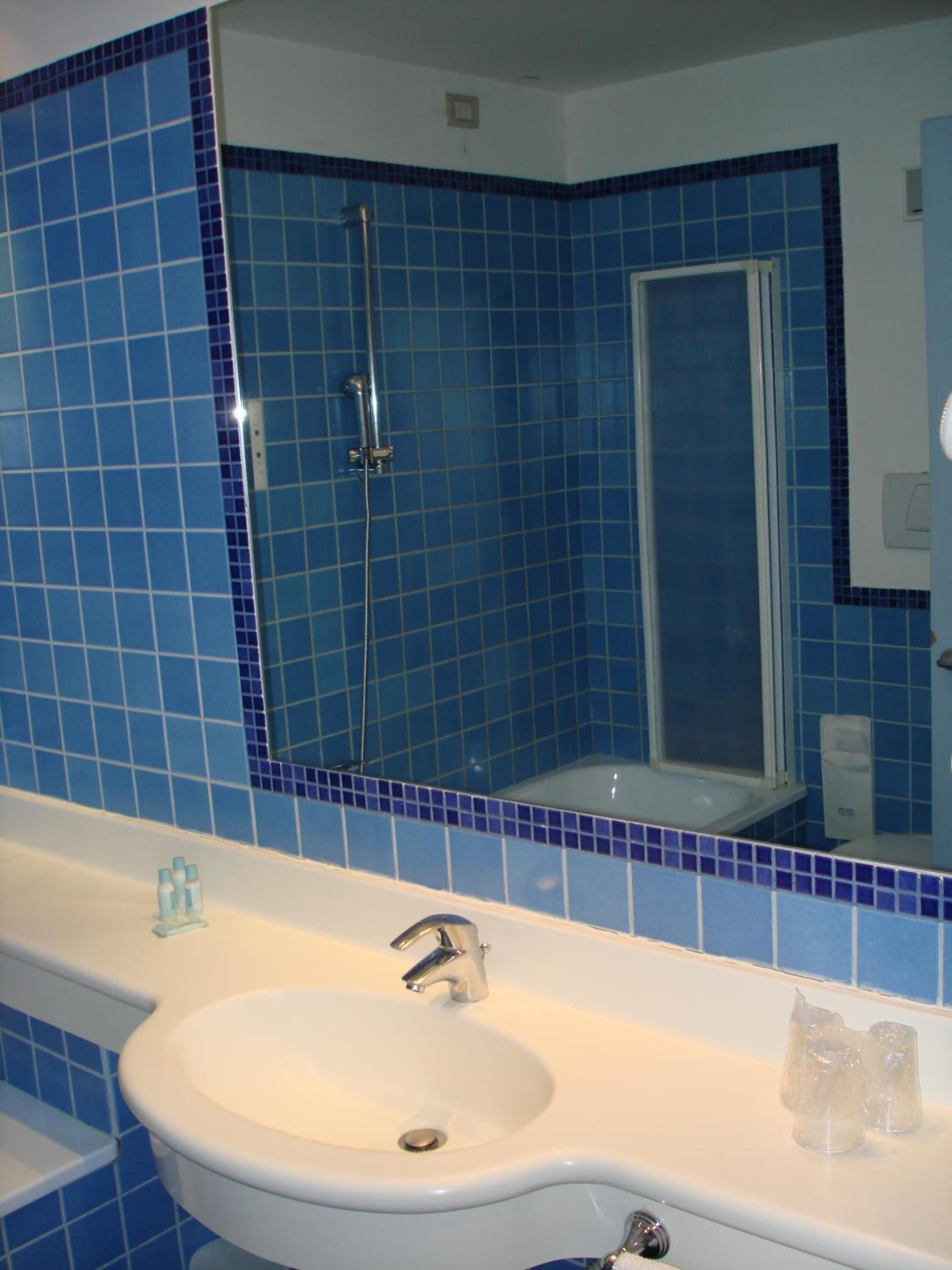 Bathroom with blue tiled walls, a white sink, and a large mirror.