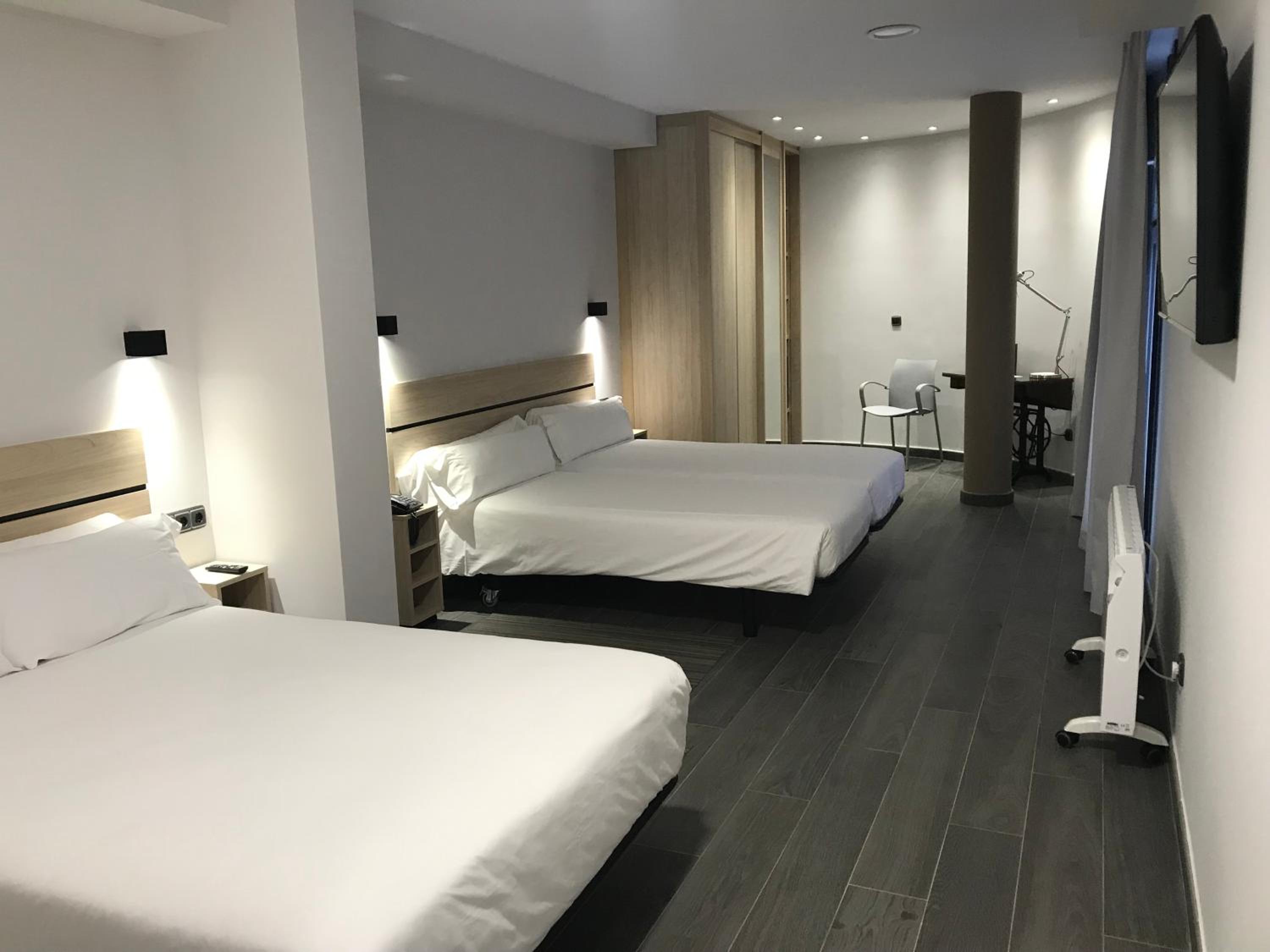 Spacious modern hotel room with two beds, wood headboards, dark floor, desk