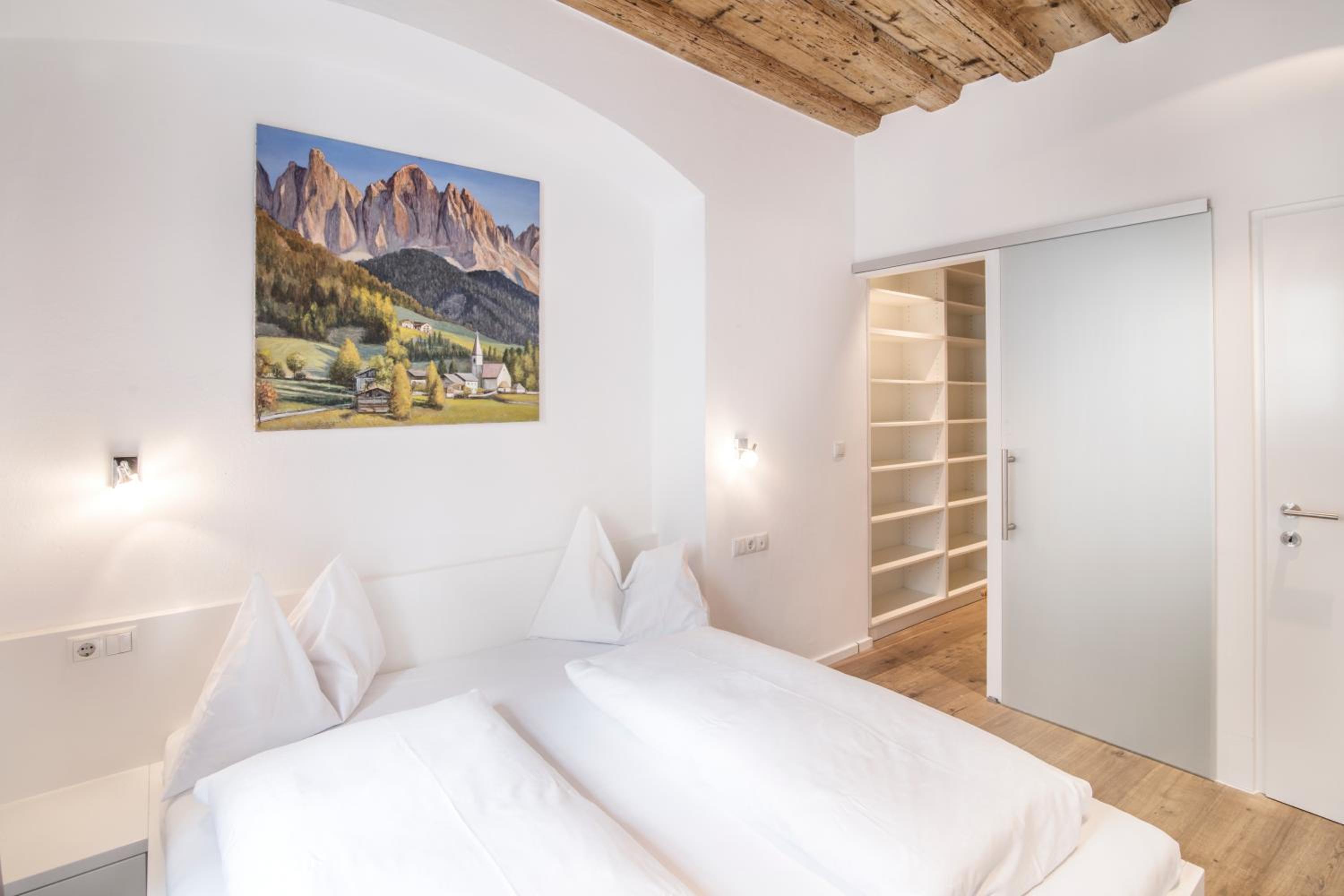 Bedroom with a white bed, wooden ceiling beams, and a landscape painting on the wall.