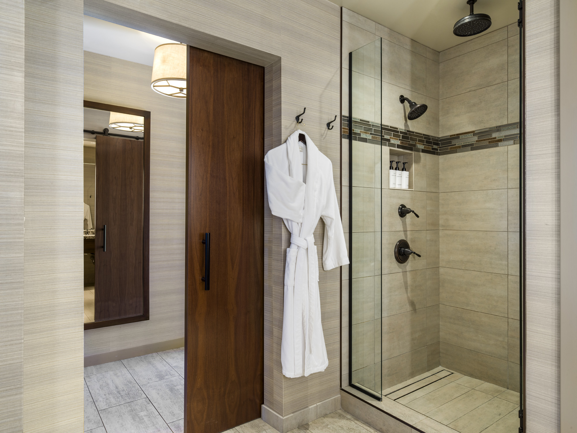 Bathroom with a glass-enclosed walk-in shower, beige tile walls, and a white robe hanging on a hook.