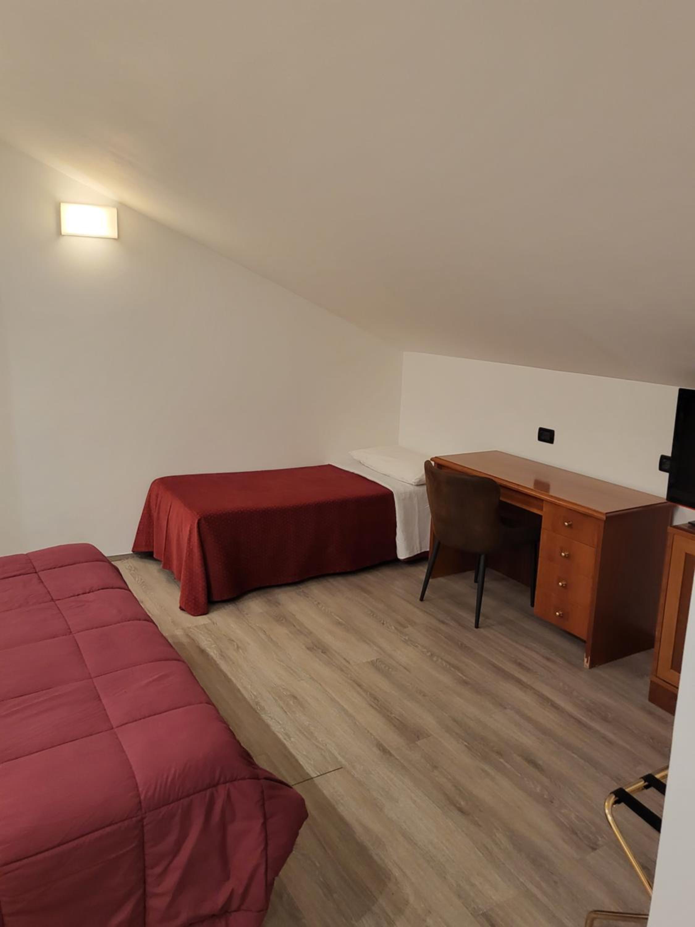 Hotel room with two beds, a wooden desk, and light wood flooring.
