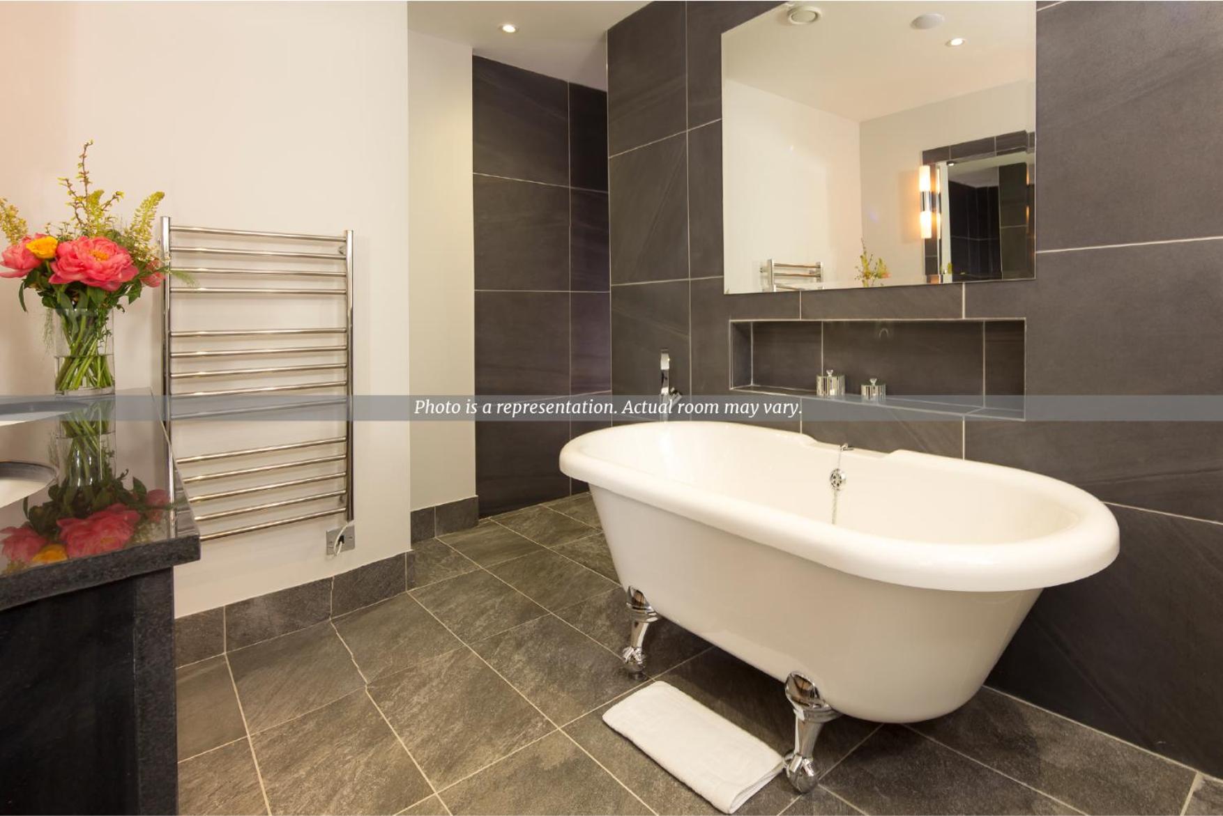 Bathroom with a white clawfoot bathtub, dark gray tiled walls, and a heated towel rack.