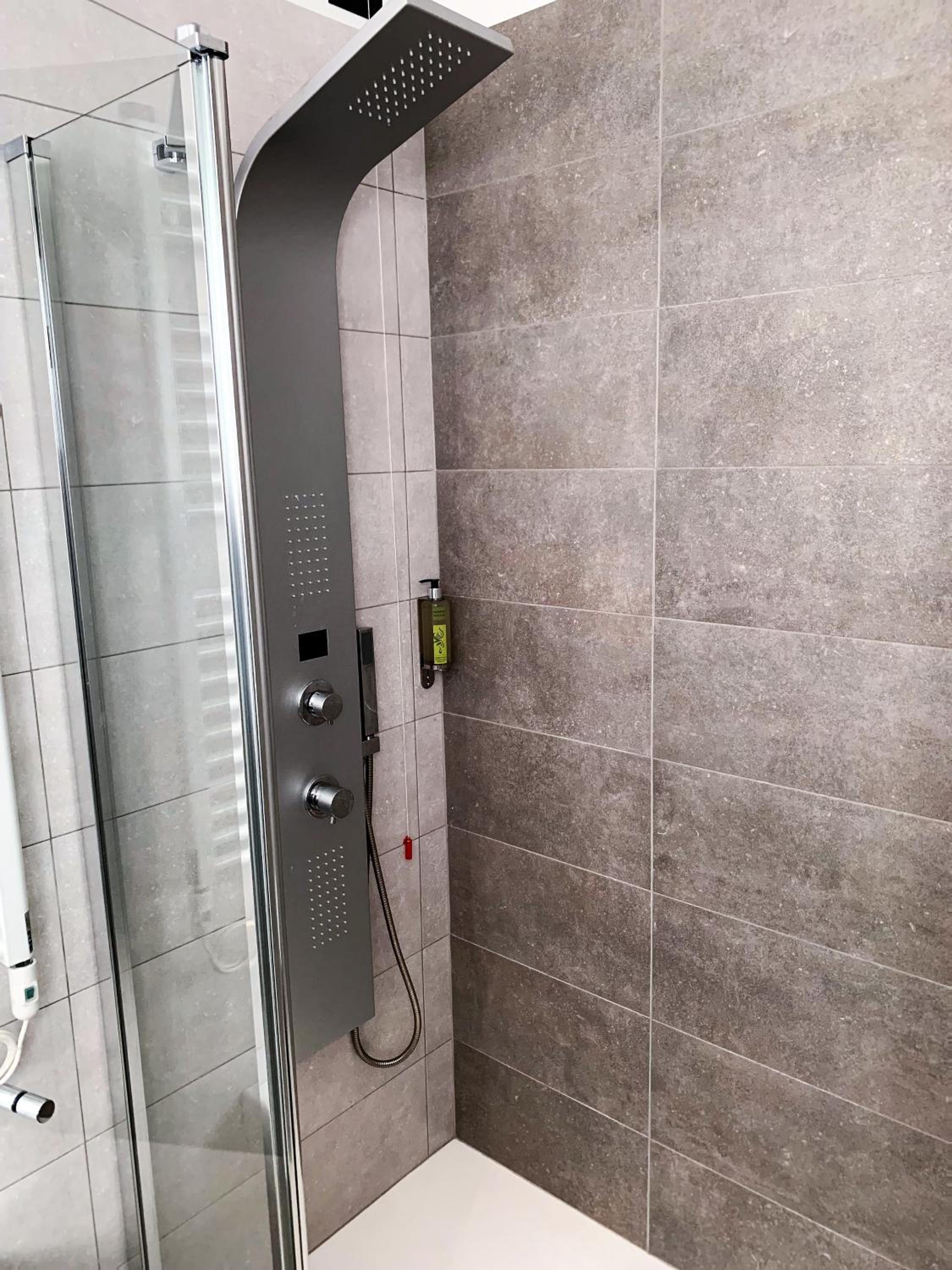 Shower with grey panel column, glass door and tiled walls