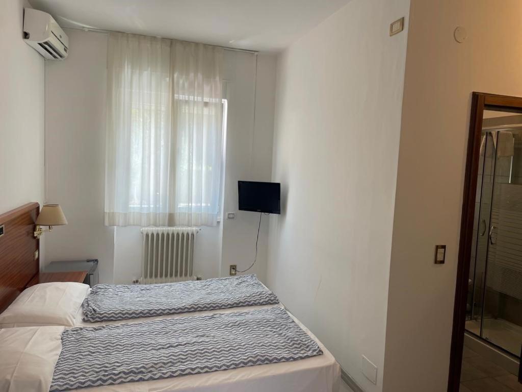 Simple hotel bedroom with bed, window, radiator, wall TV and shower