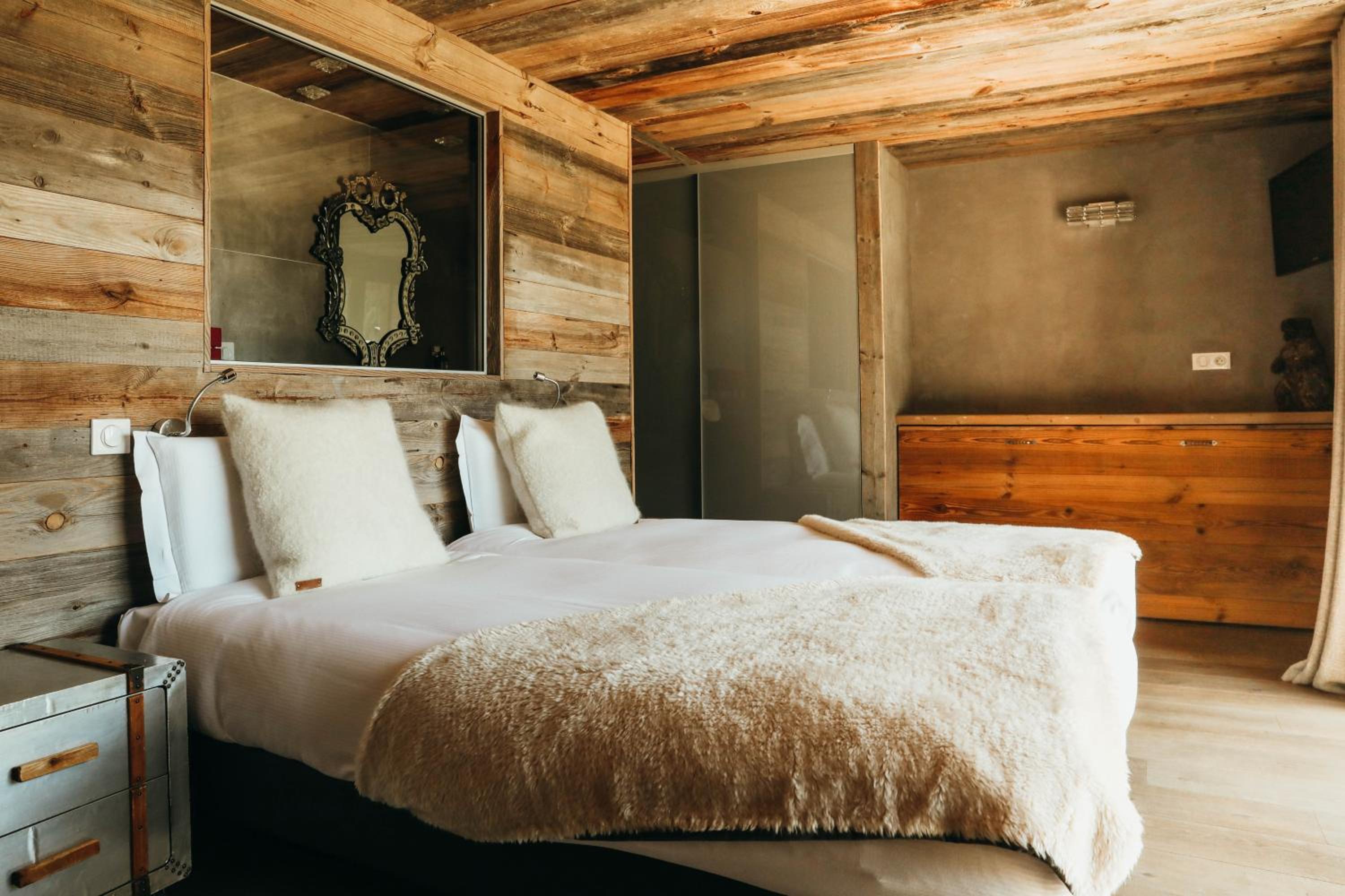 Bedroom with a double bed, white linens, and a wooden wall with a mirror.