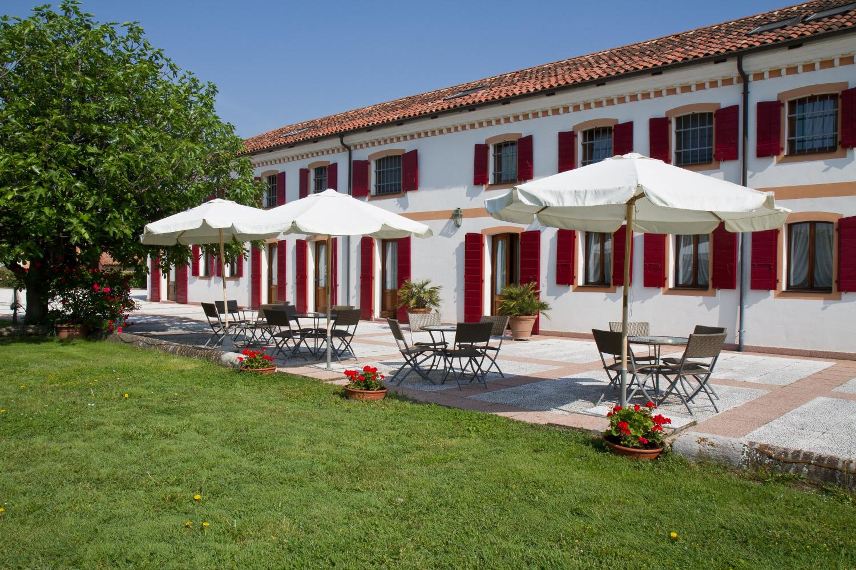 Outdoor patio with white umbrellas, black chairs, and tables in front of a white building with red shutters.