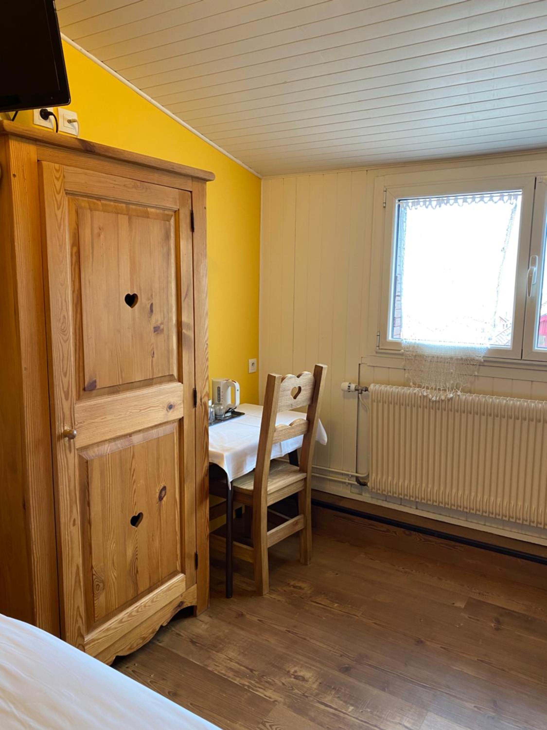 Hotel room corner featuring a wooden wardrobe, small dining table, and yellow accent wall.