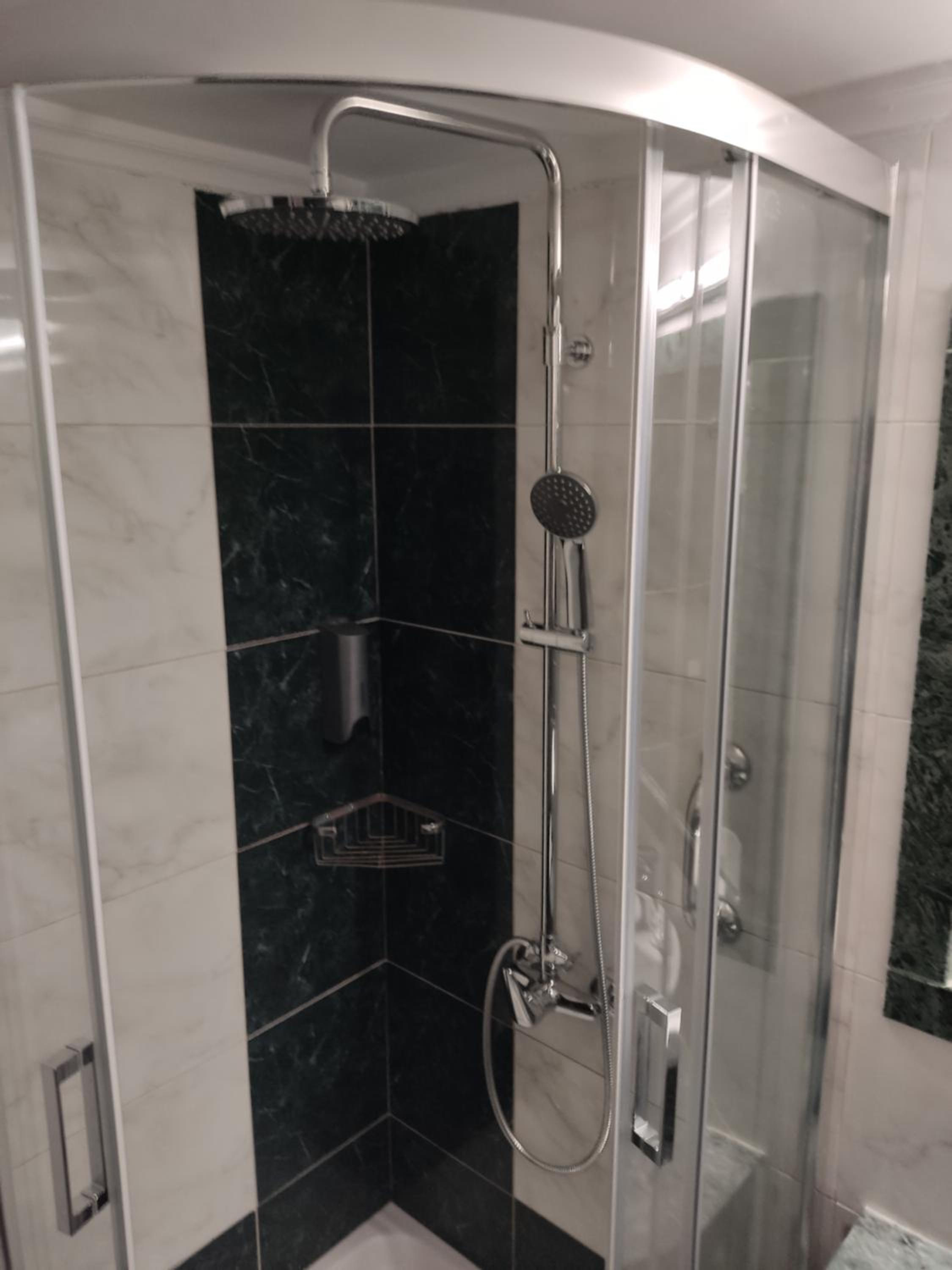Bathroom shower with glass enclosure, black marble accent wall, and chrome fixtures.