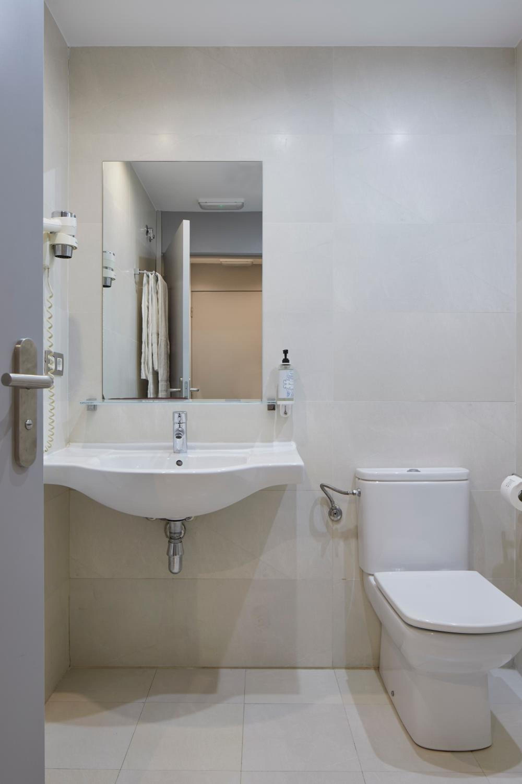 Bright tiled bathroom with wall-mounted sink, mirror, hairdryer and toilet