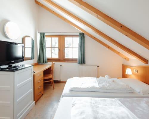 Attic bedroom with wooden beams, twin beds, desk and TV