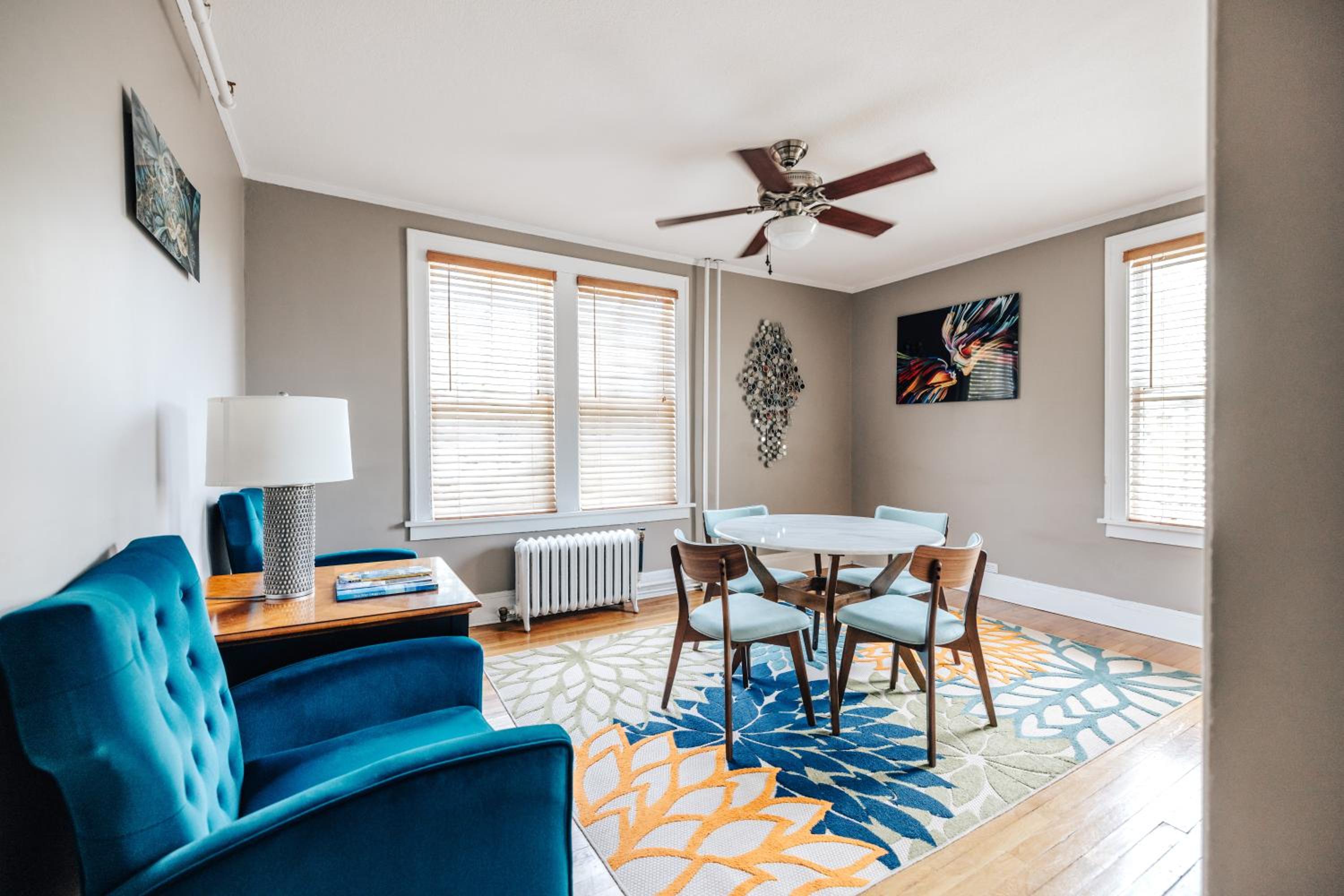 Bright living and dining area with teal armchairs, round table, colorful rug