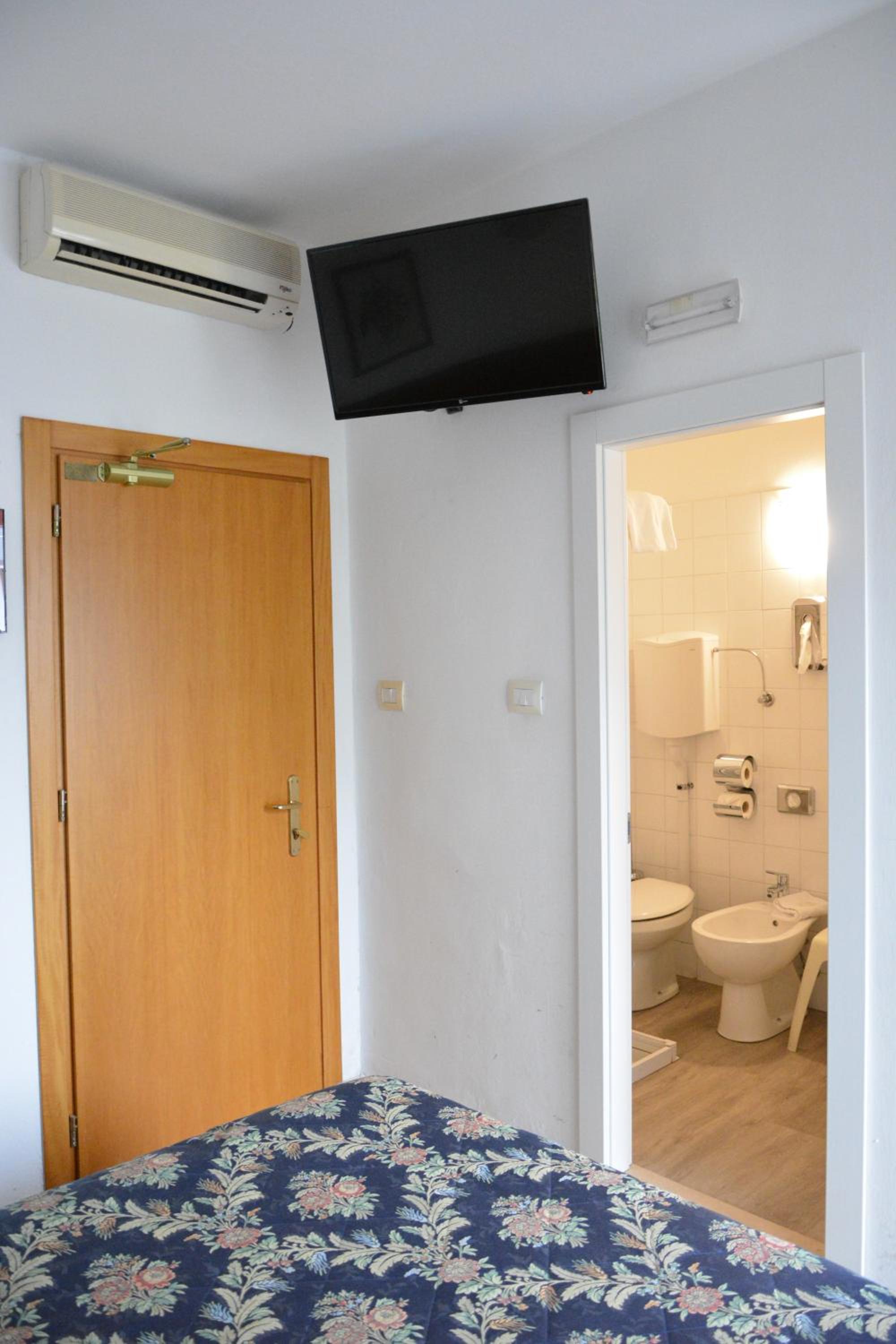 Hotel room with a floral bedspread, wall-mounted TV, and an open door to a tiled bathroom.