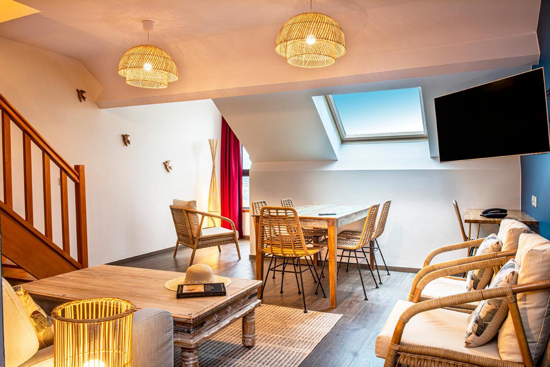 Attic living and dining area with rattan furniture, skylight, wall-mounted TV and staircas