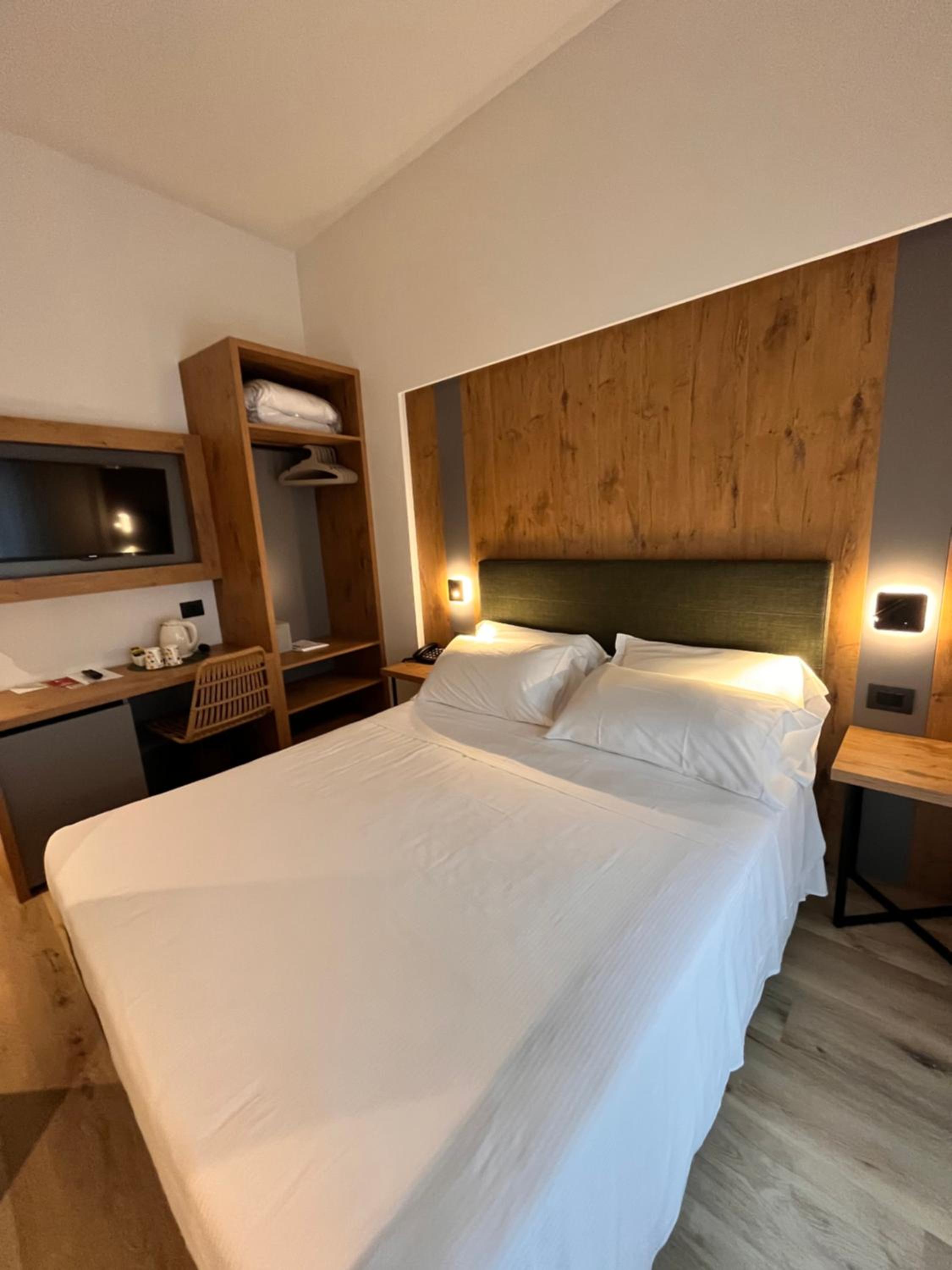 Hotel bedroom with double bed, wooden headboard panel, desk and wall-mounted TV