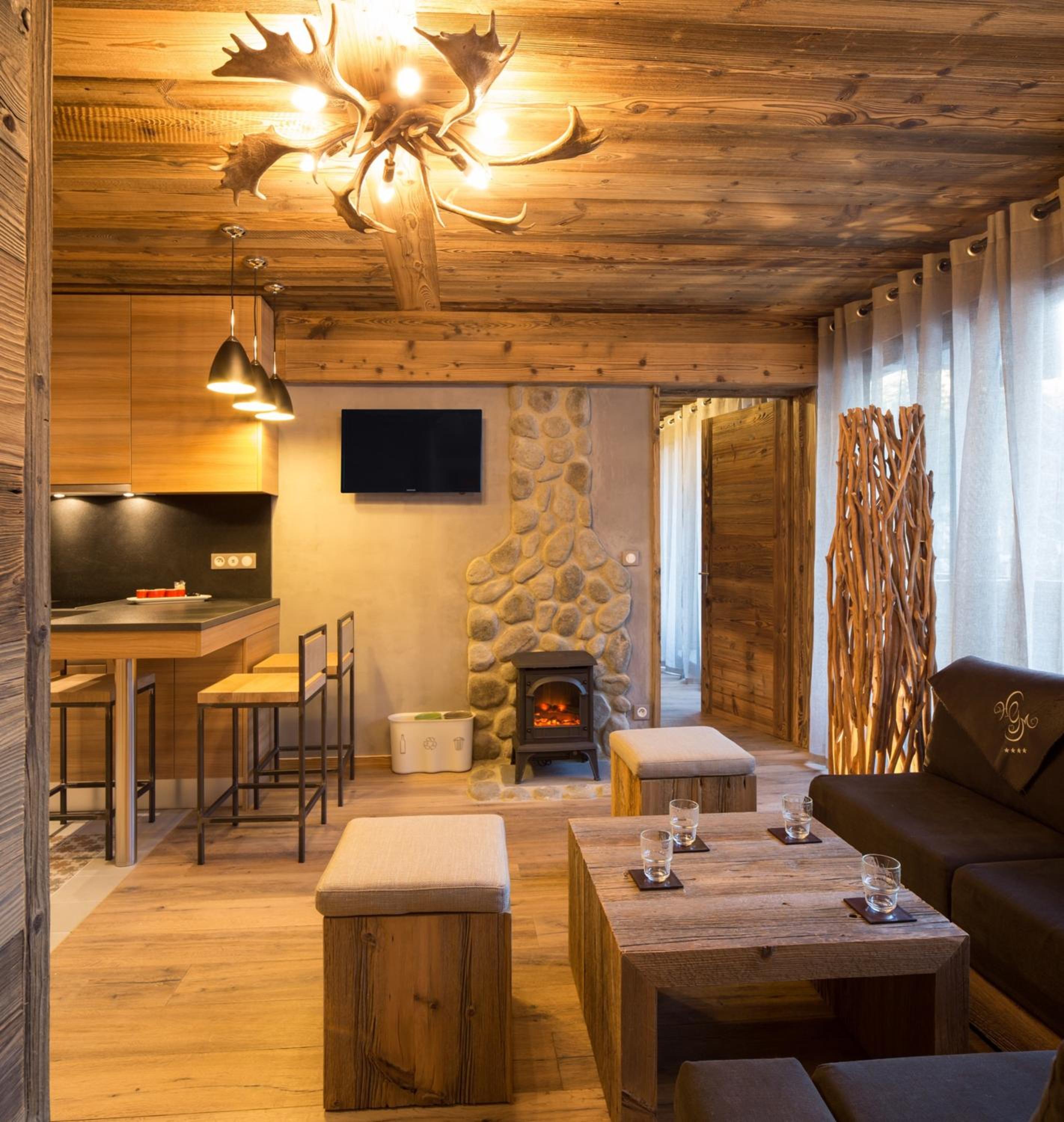 Wood-paneled living area with a stone fireplace, dark sofa, and rustic antler chandelier.