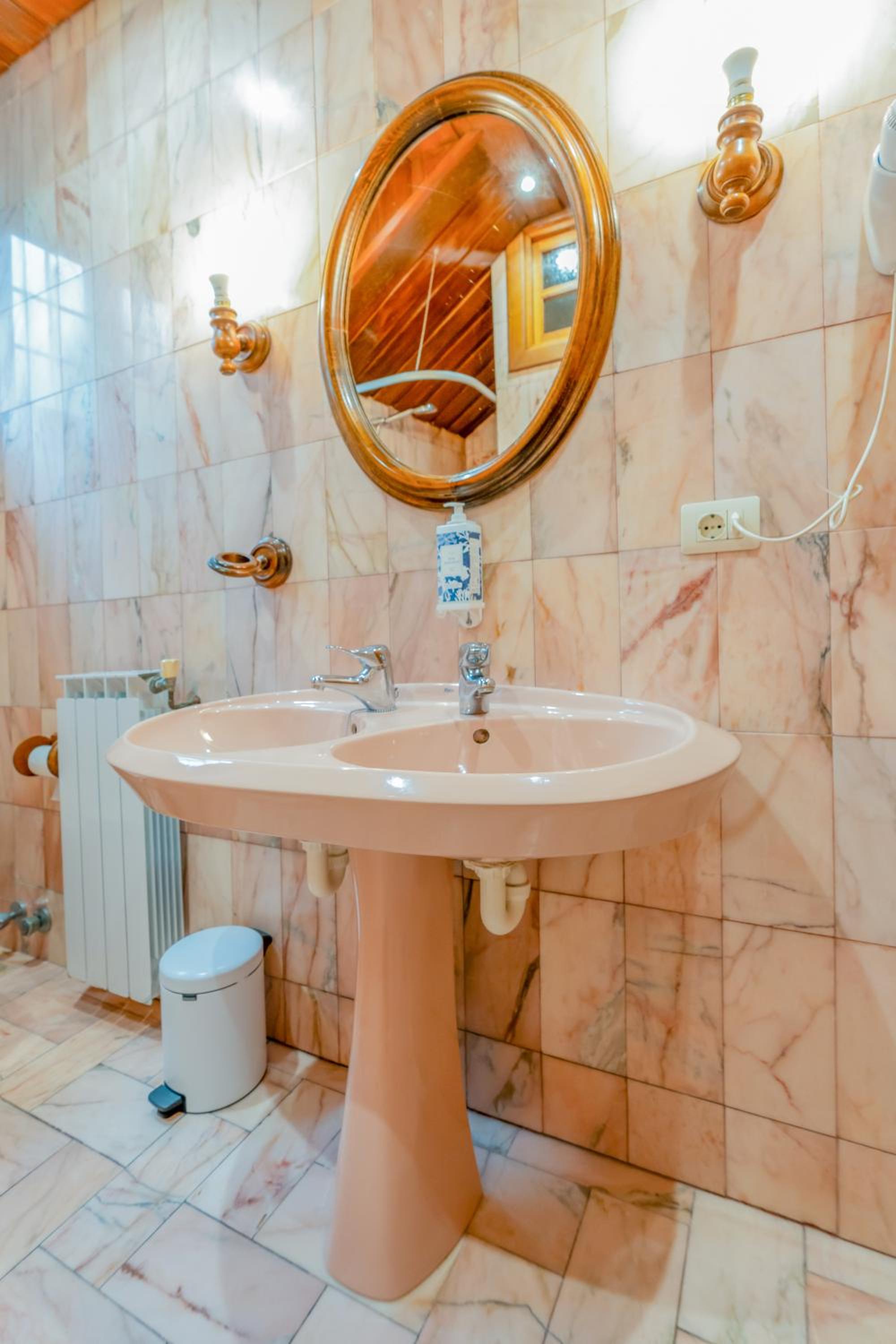 Bathroom with a double pedestal sink, marble tile walls, and a round mirror.