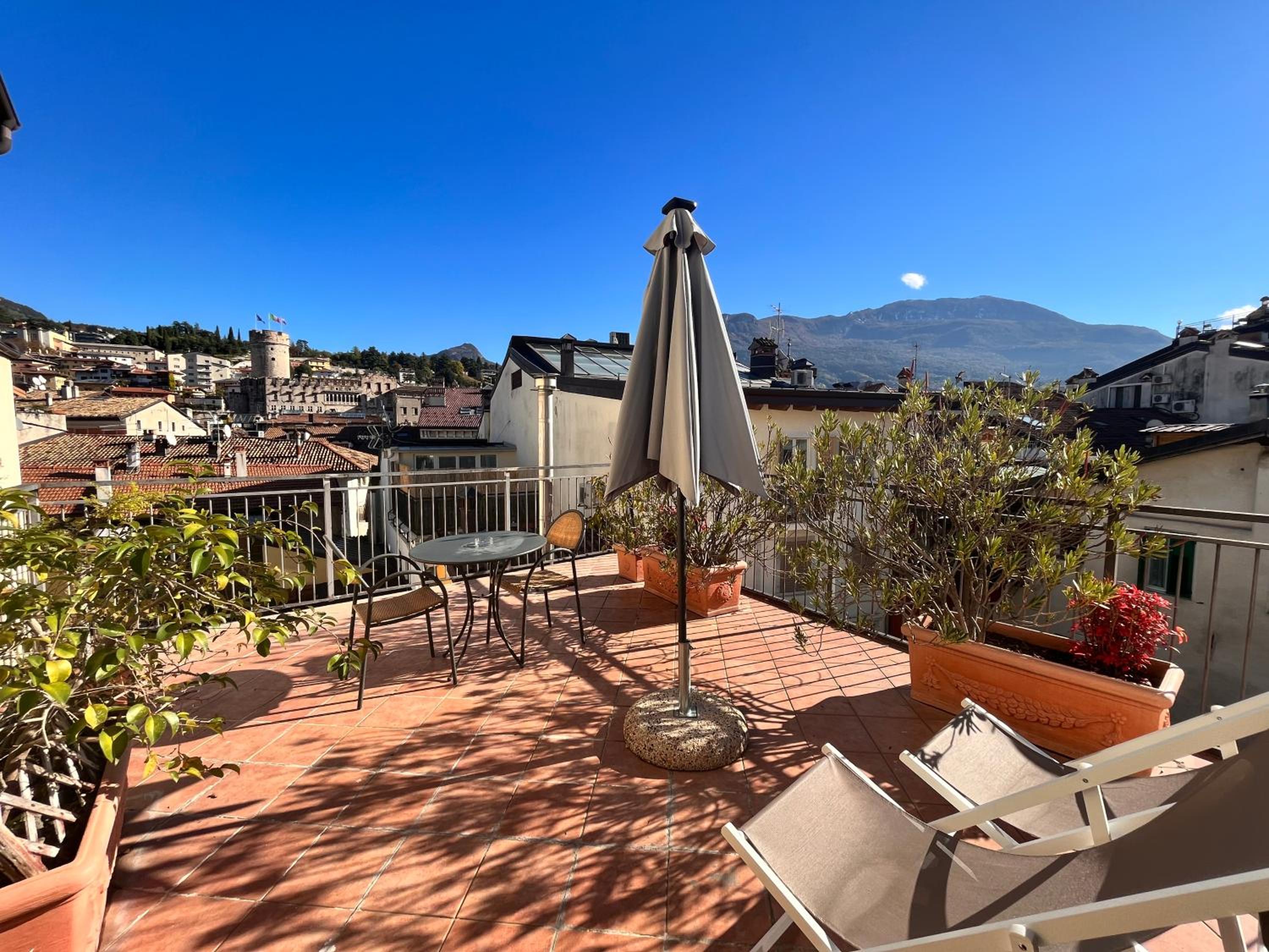 Sunny rooftop terrace with bistro table, lounge chairs, potted plants, mountain and town v