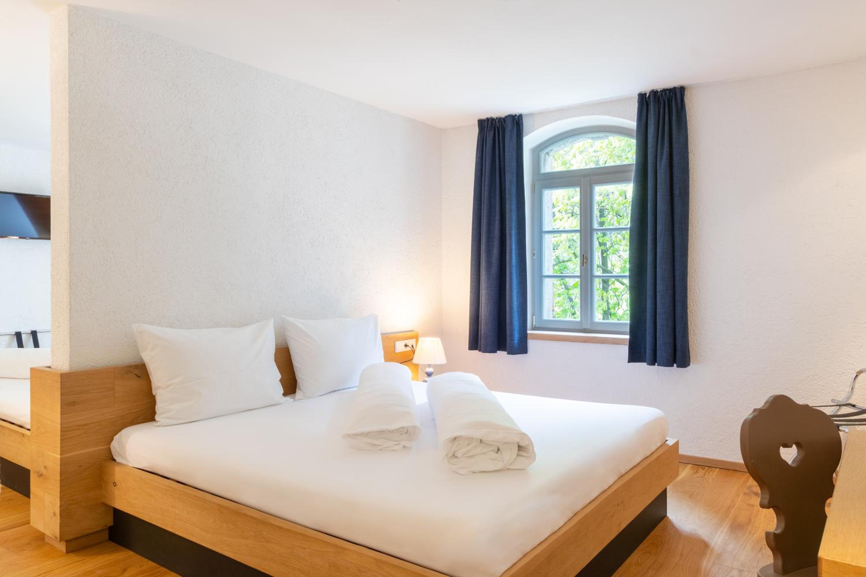 Double bed with rolled duvets beside arched window with navy curtains