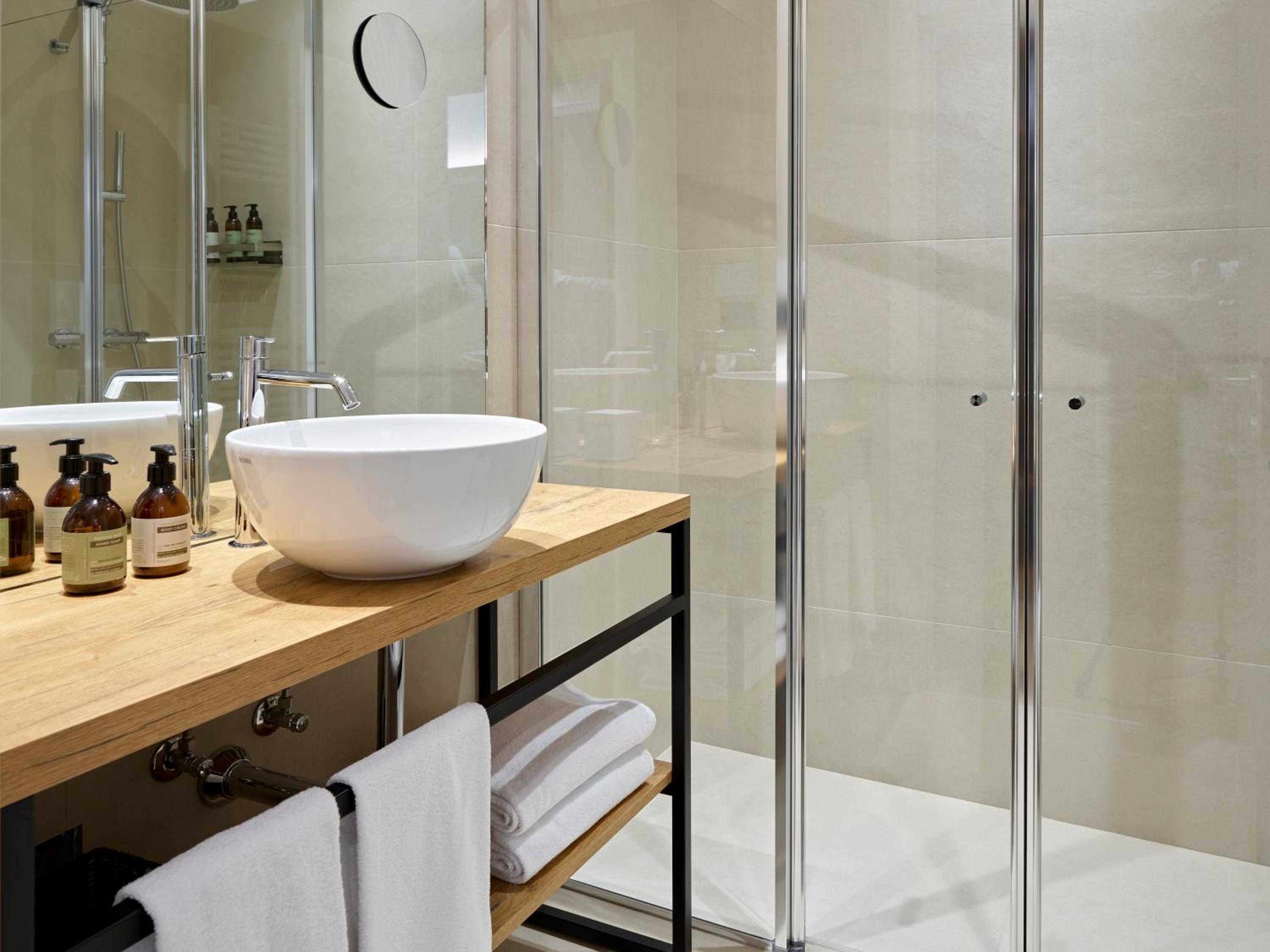 Bathroom vanity with vessel sink, toiletries, towels and glass-enclosed shower
