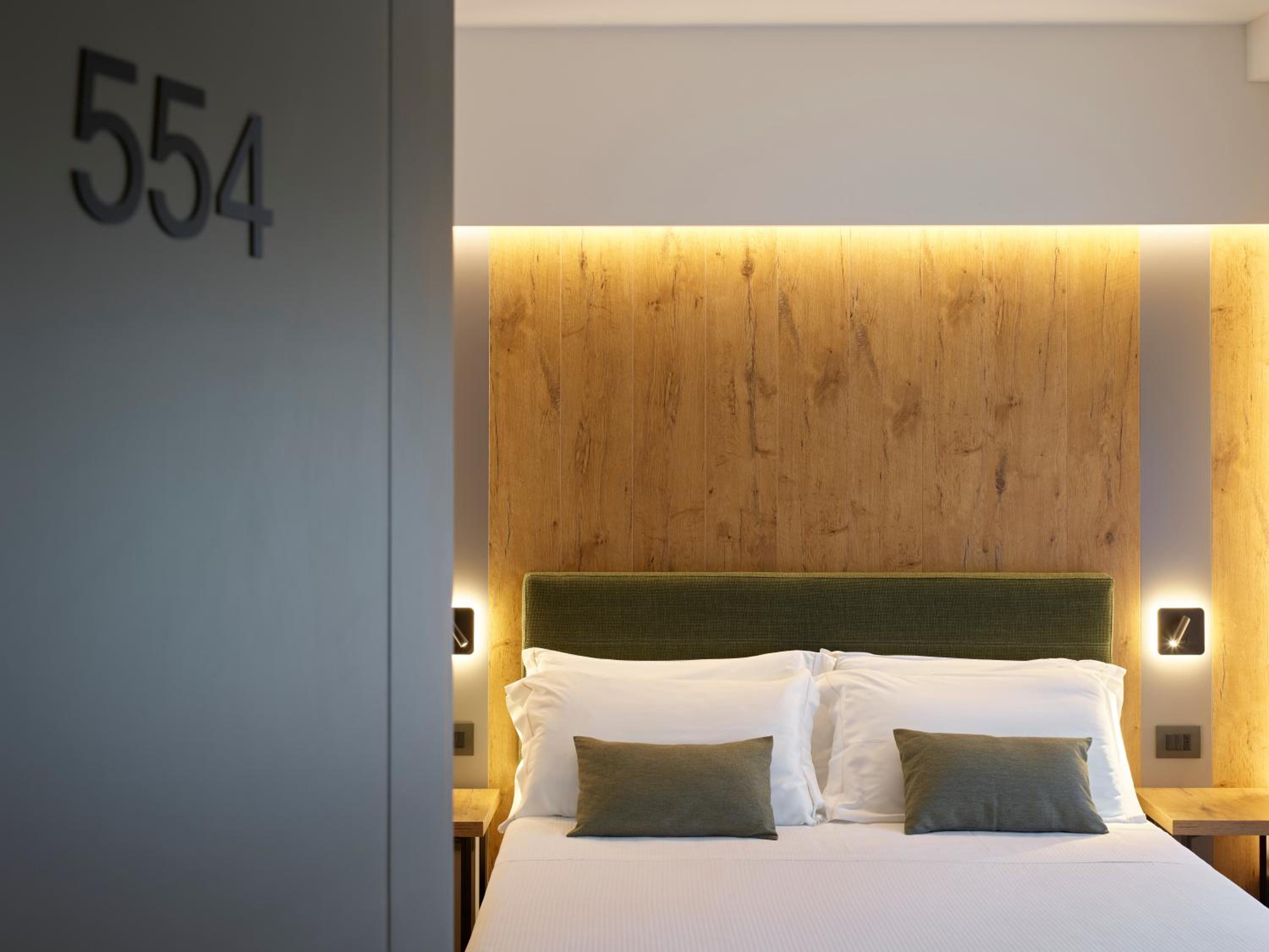 Hotel bedroom with wood headboard wall, green upholstery, white bedding, room number 554