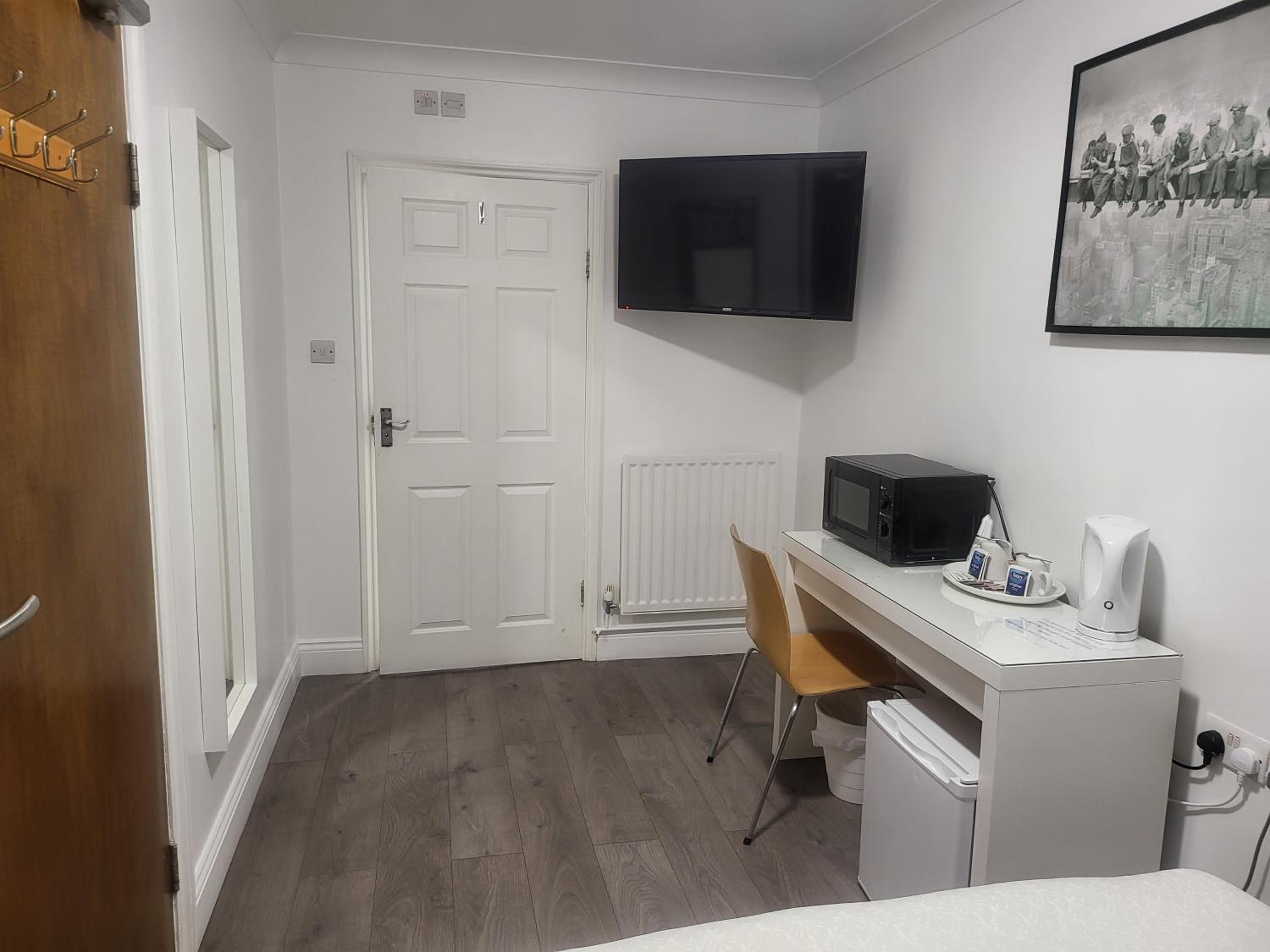 small room with a desk, tv, and refrigerator