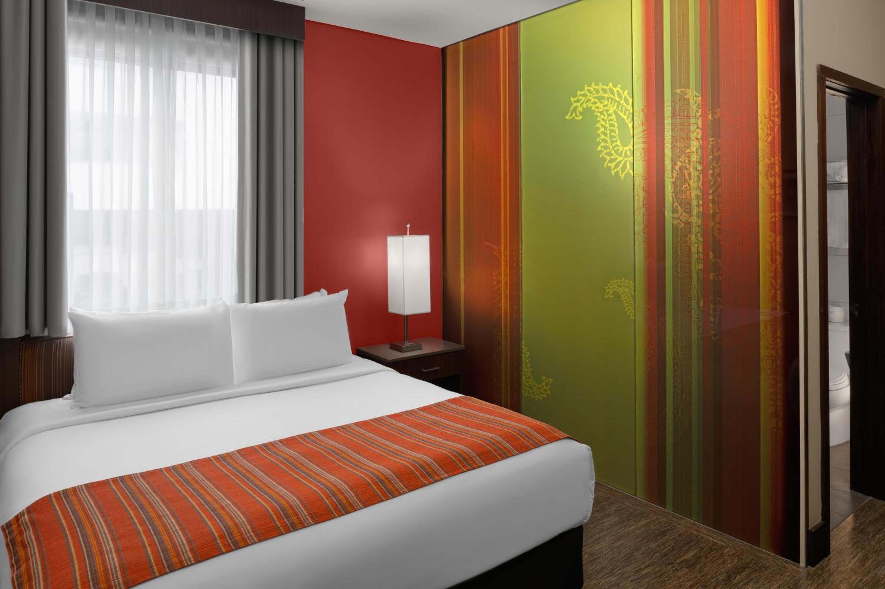 Hotel room with a double bed, red accent wall, and colorful patterned partition.
