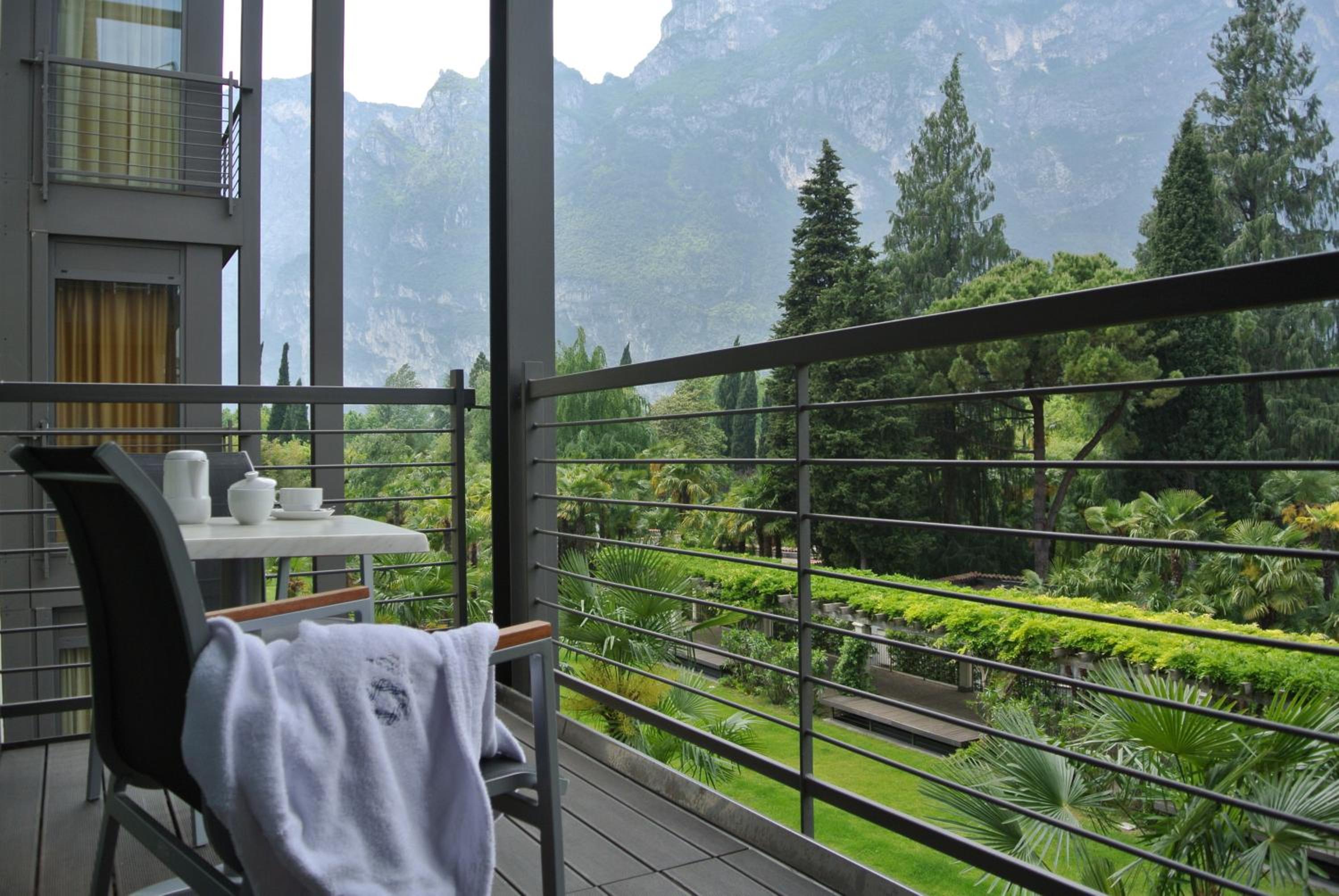 Hotel balcony with a table, chairs, and a view of mountains and greenery.