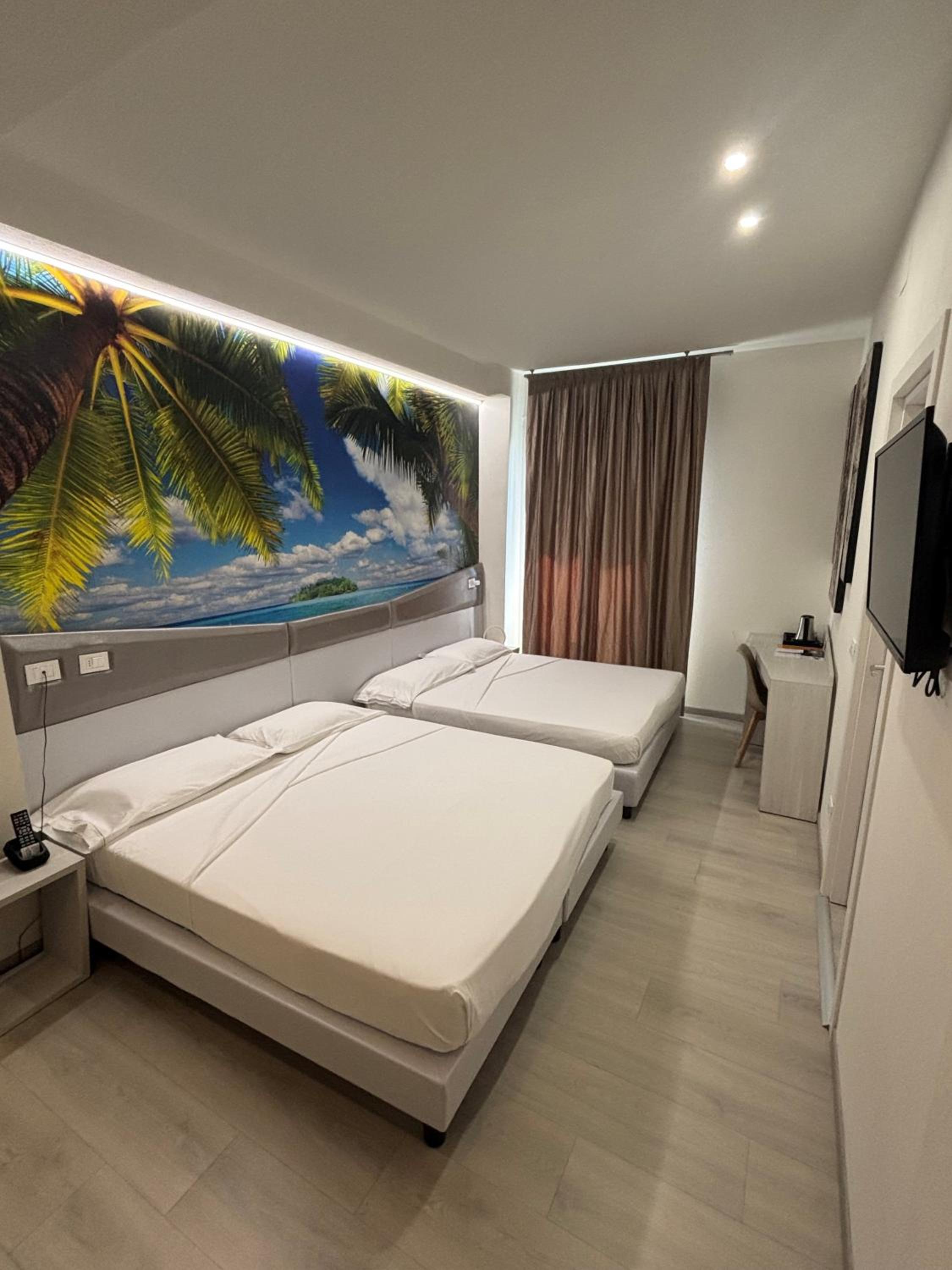 Hotel room with two white beds and a large palm tree mural on the wall.