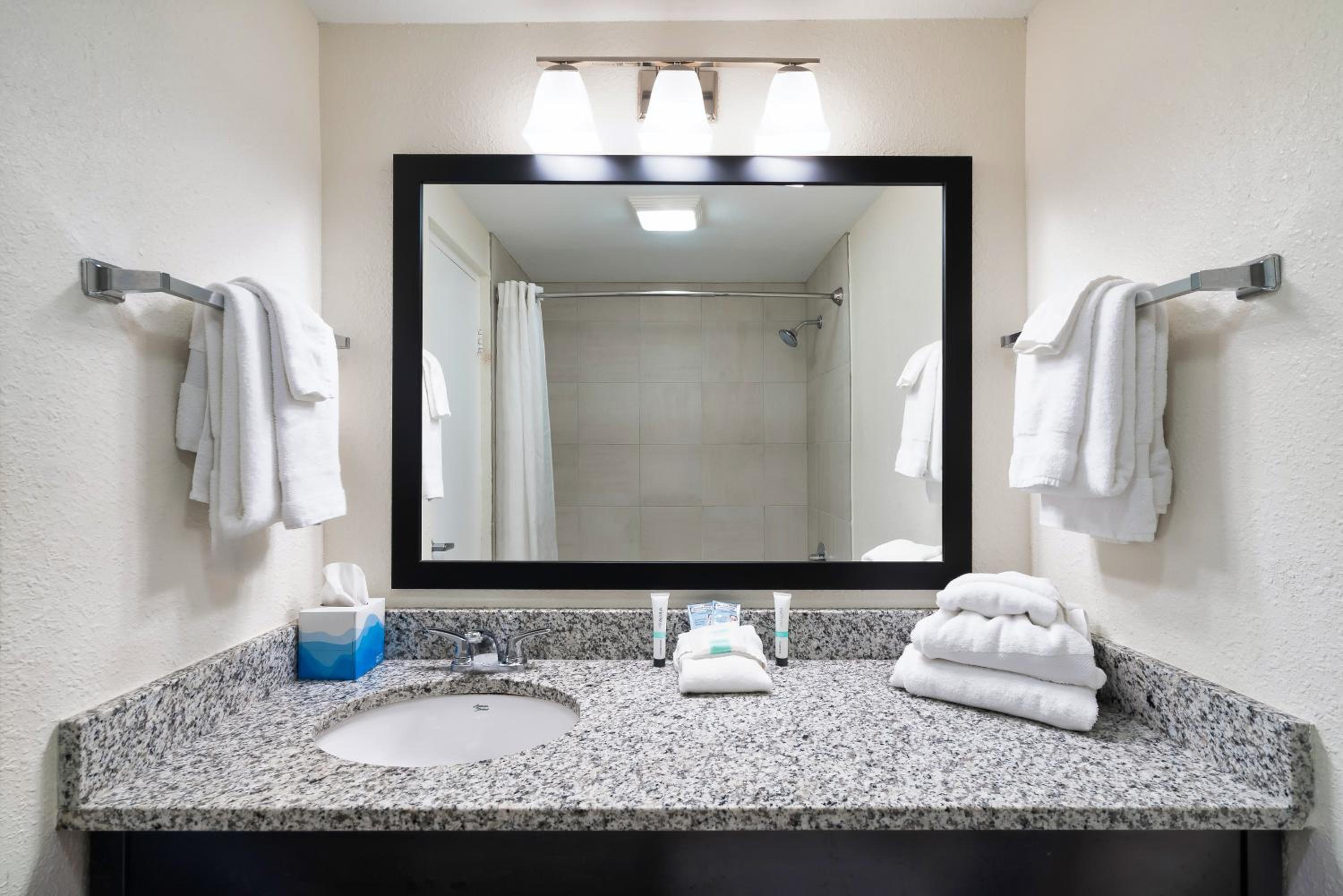 Bathroom granite vanity with sink, large mirror, towels, and shower reflected