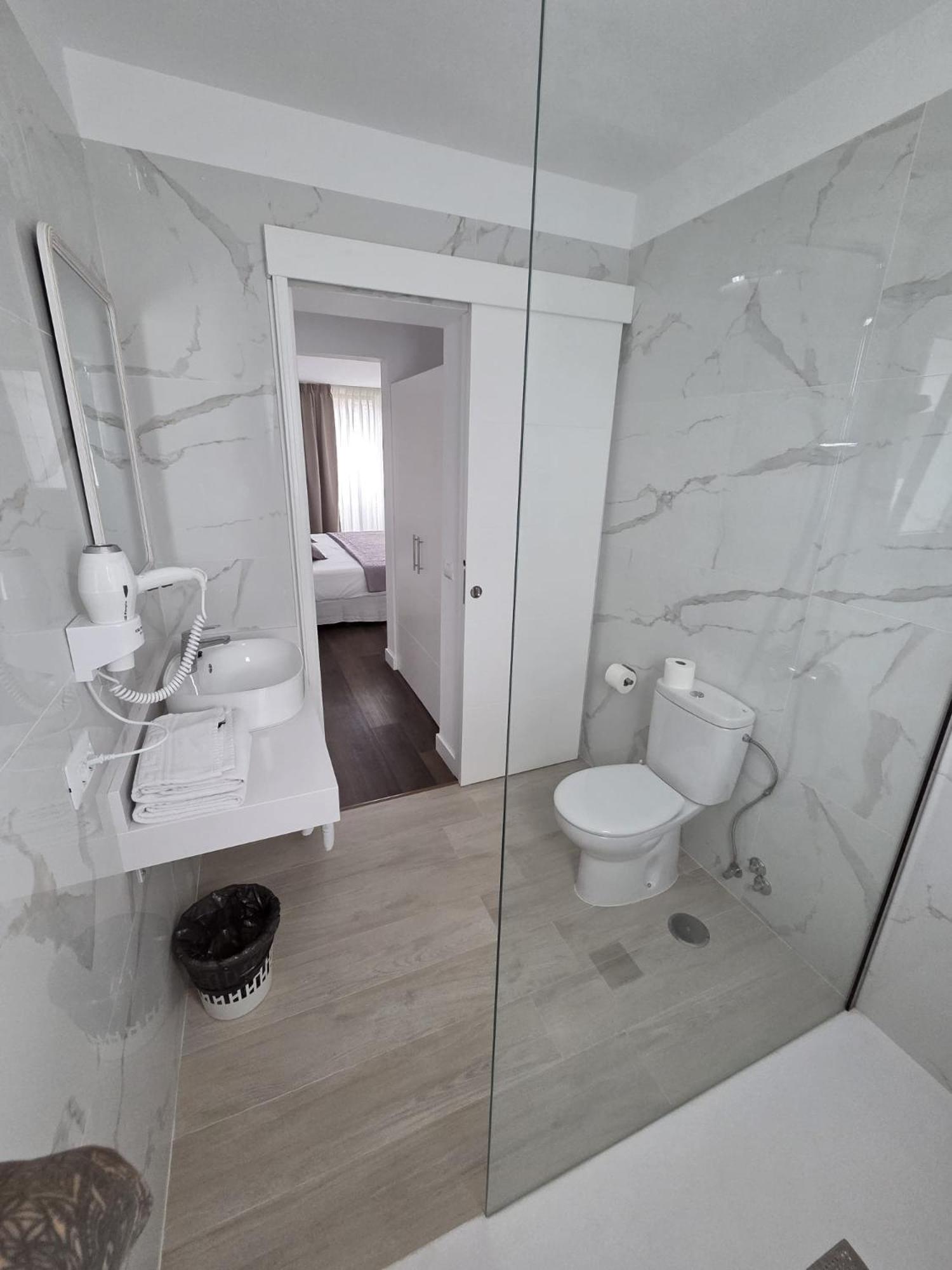 Bathroom with marble walls, white toilet, sink, and glass shower partition.