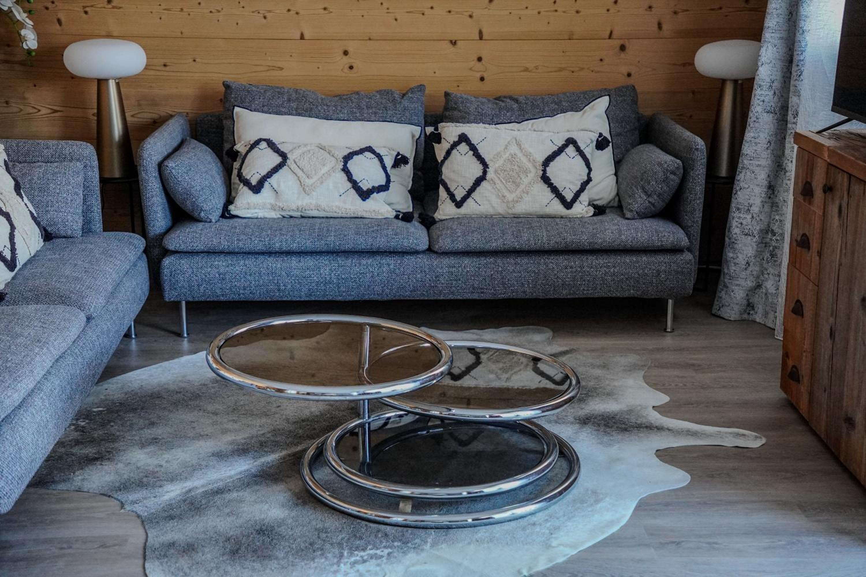 Grey sofas, chrome swivel coffee table and cowhide rug in wood-paneled lounge