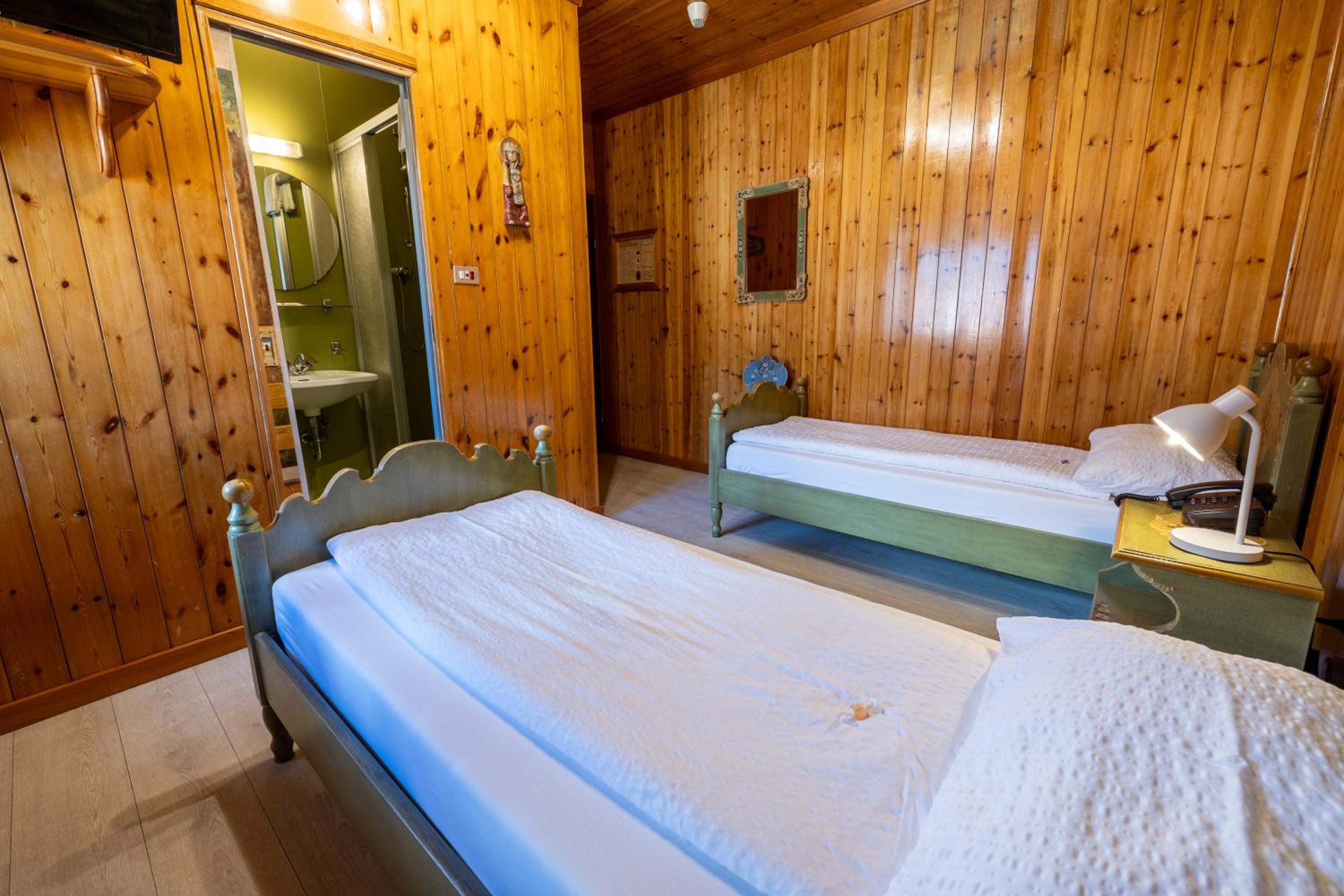 Wood-paneled twin room with green painted single beds and ensuite bathroom
