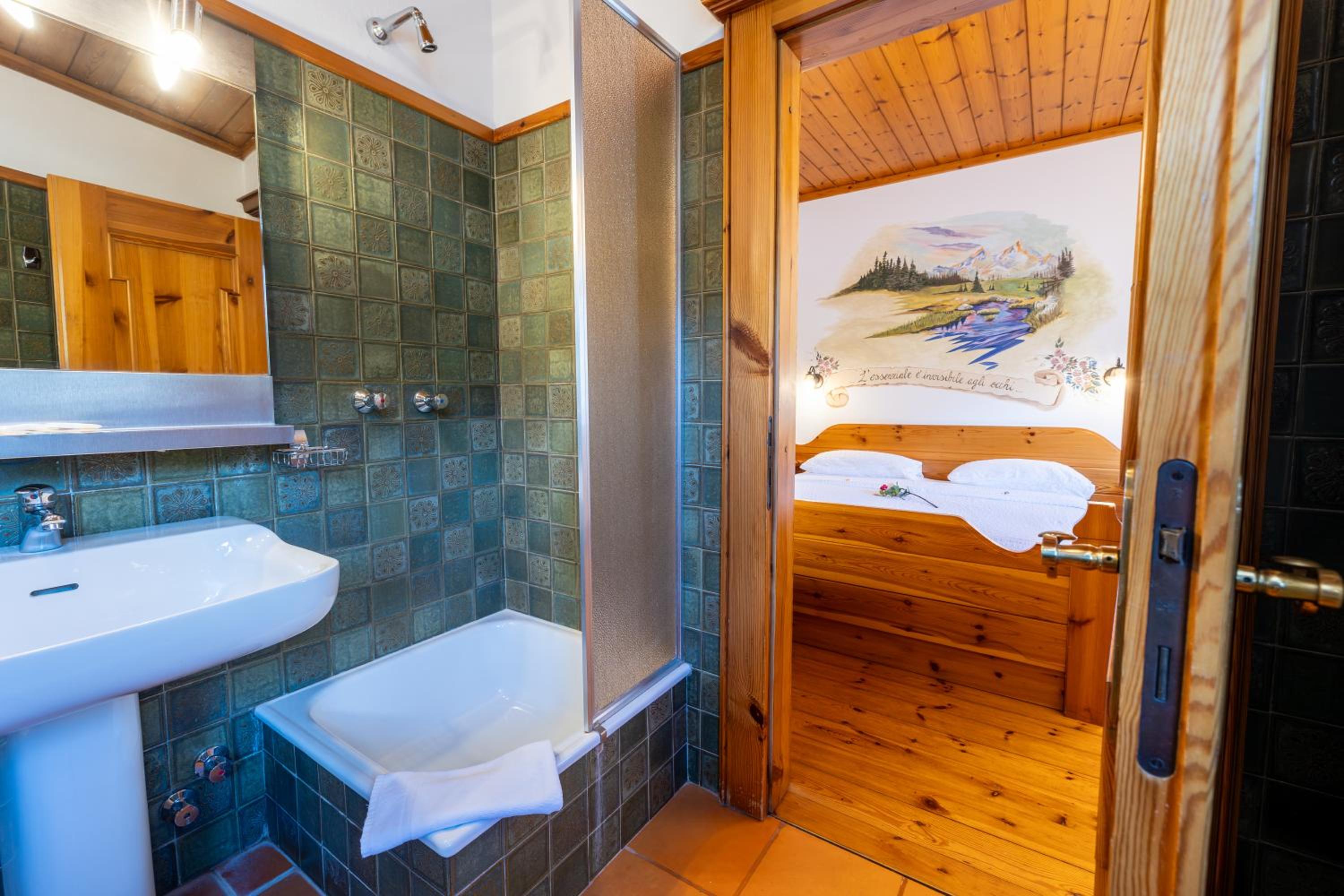 Green-tiled bathroom with sink and tub, wooden alpine bedroom visible beyond