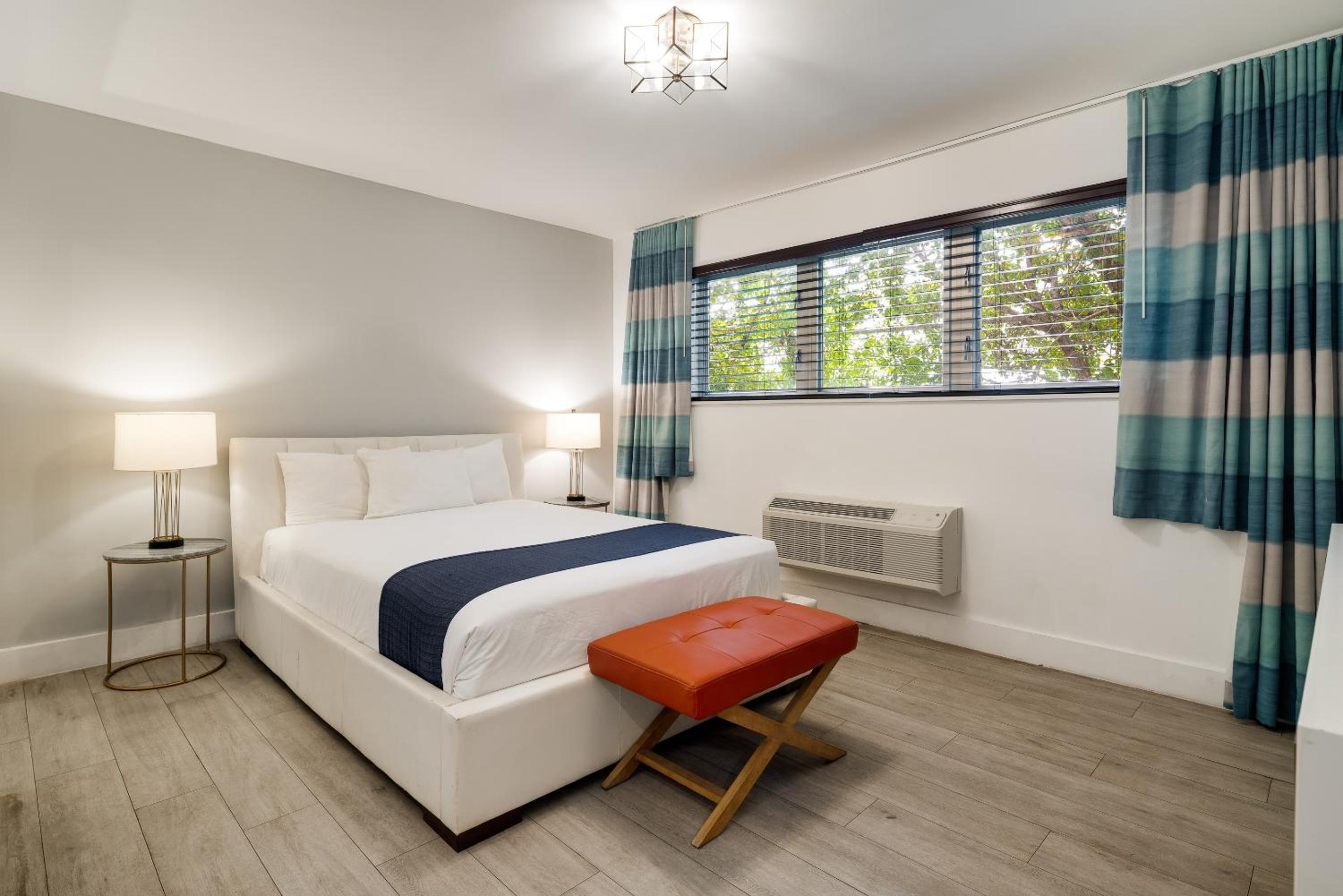 Bedroom with a white bed, blue runner, and an orange bench at the foot.